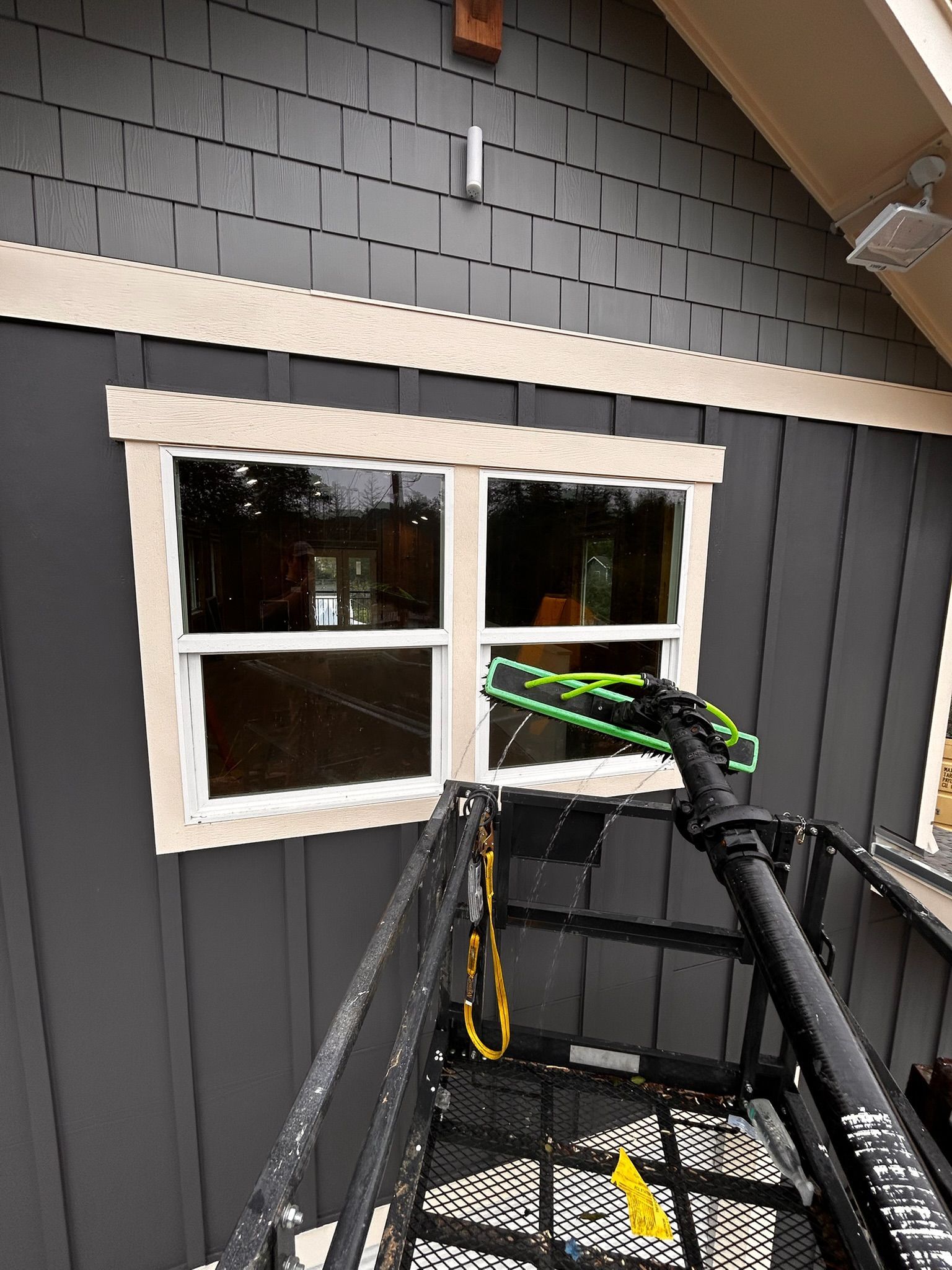 Window being cleaned from a lift, gray siding, white trim.