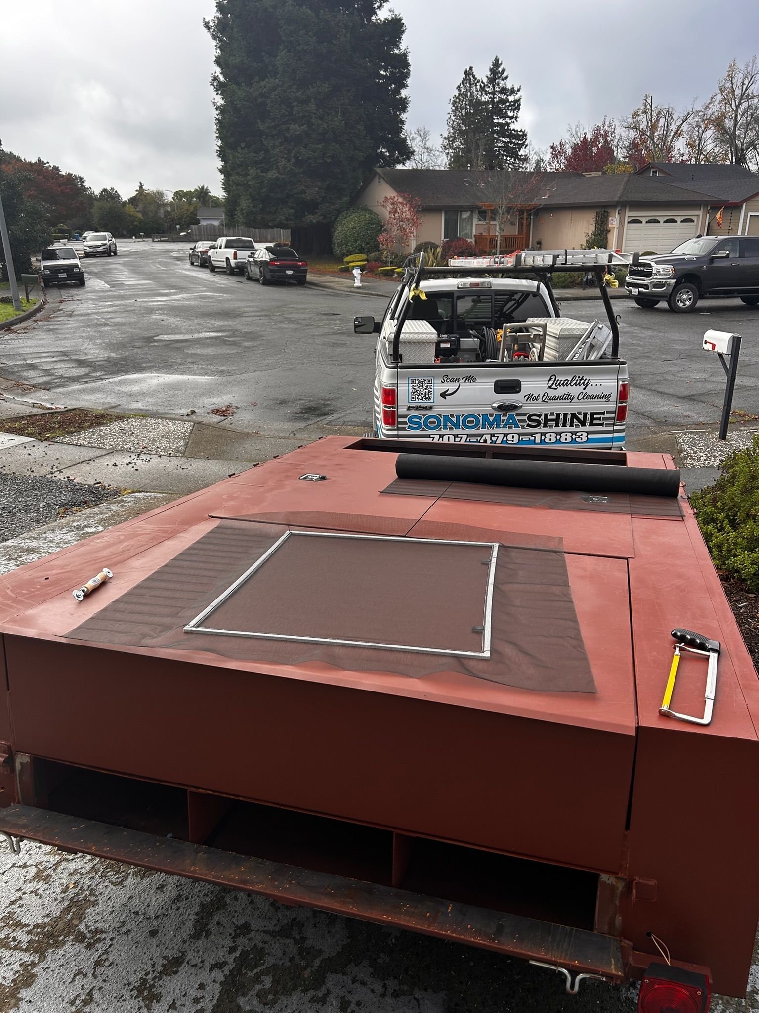 Red trailer with a brown platform, parked in a residential street; a truck is hooked up.