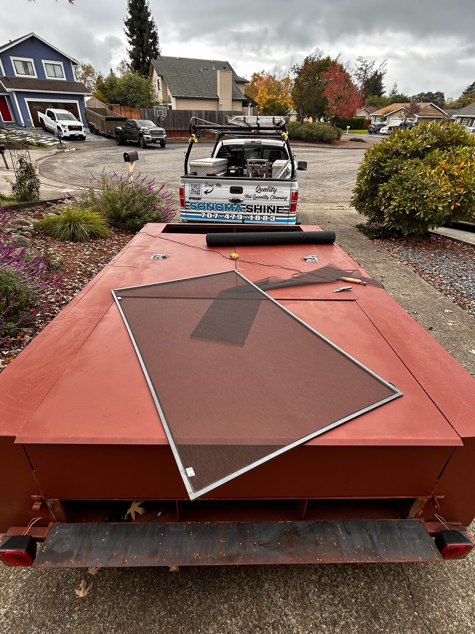 Red trailer with screen resting on top, parked behind a white pickup truck in front of suburban homes.