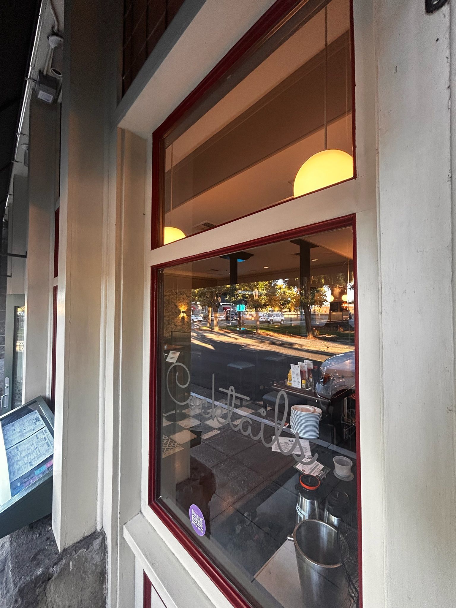 Exterior view of a window reflecting a city street and the interior of a business with bright overhead lights.