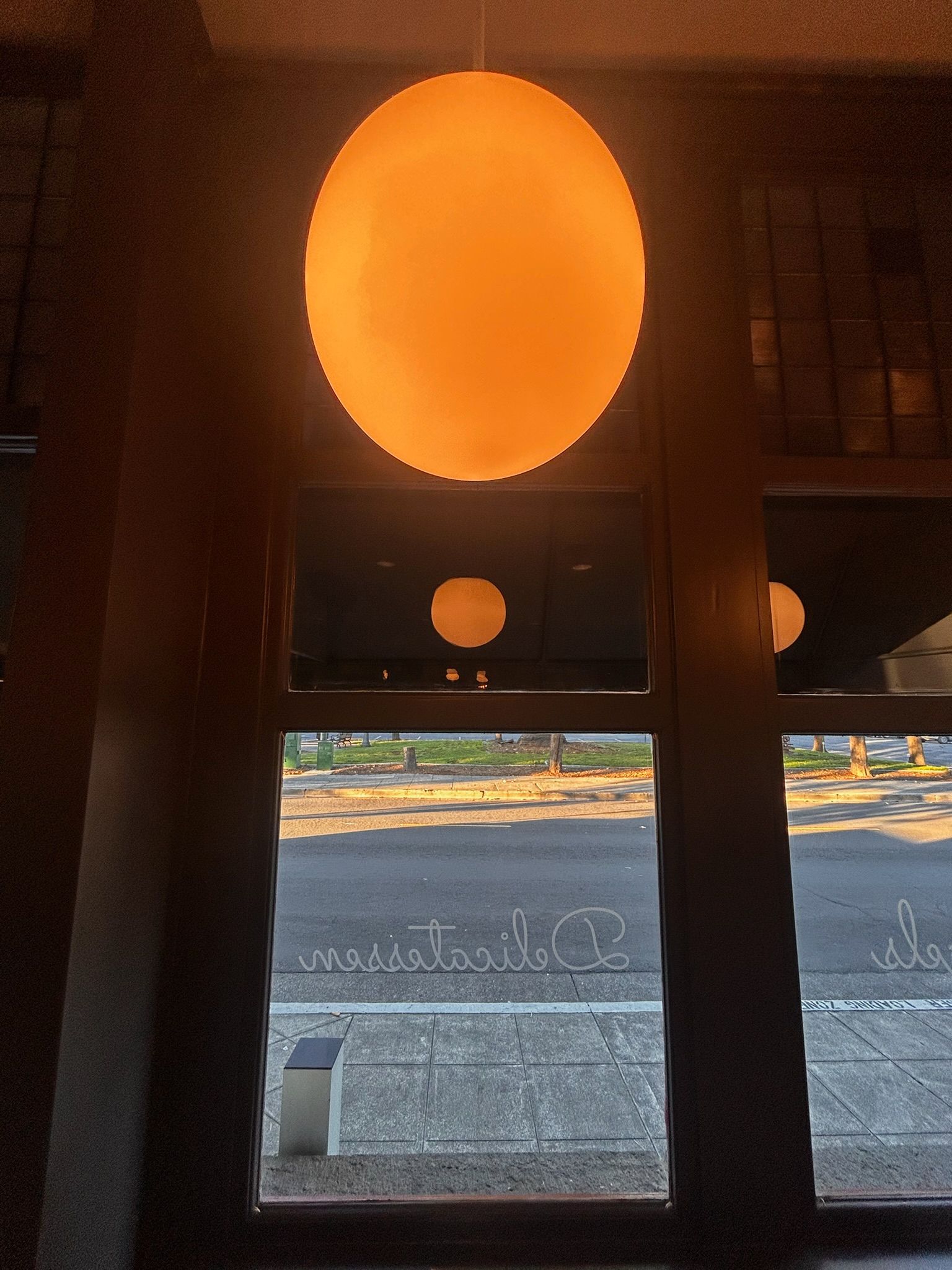 Large orange orb light fixture inside building, reflected in window overlooking street.