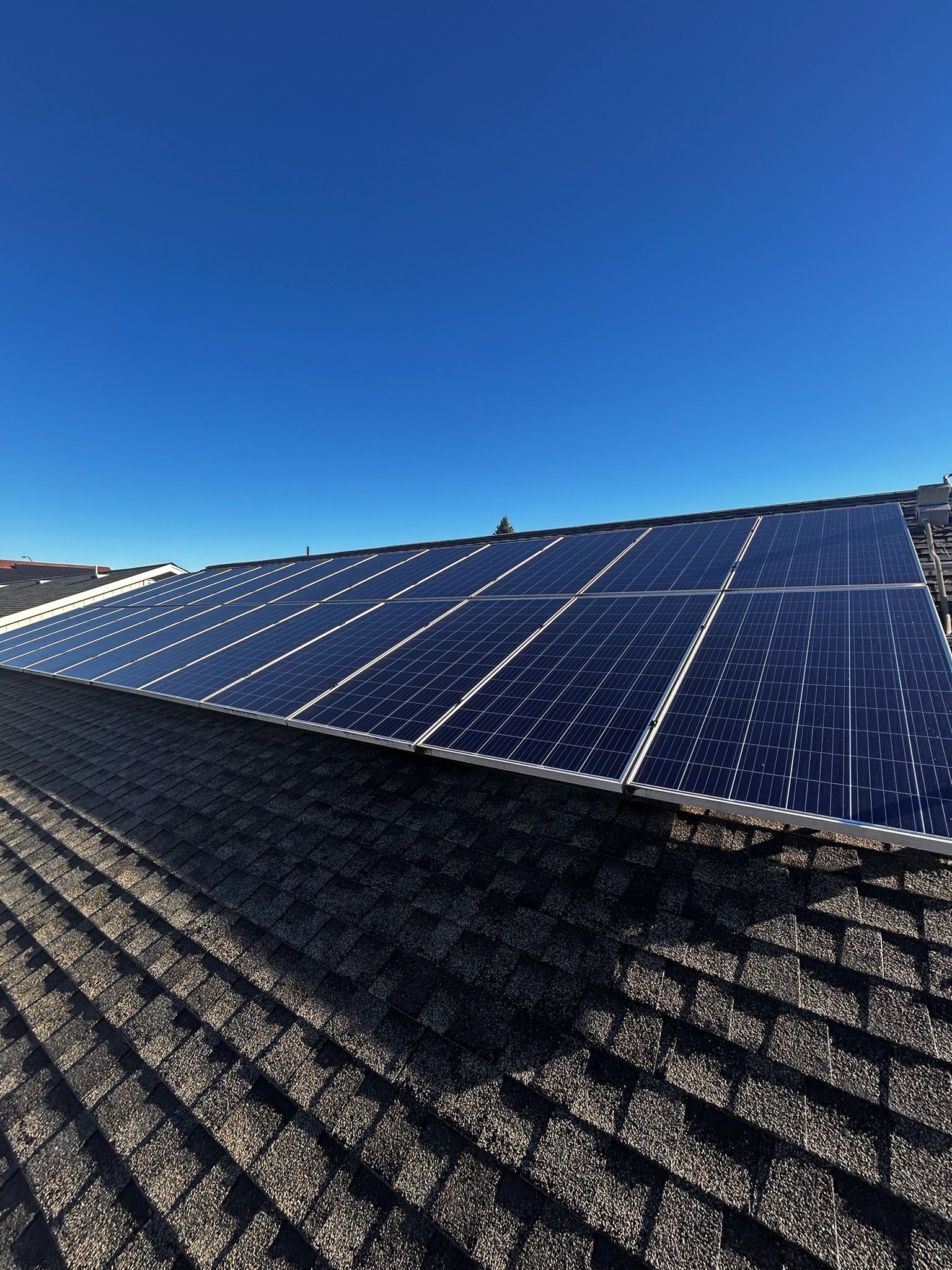 Solar panels installed on a dark-shingled roof under a clear, bright blue sky.