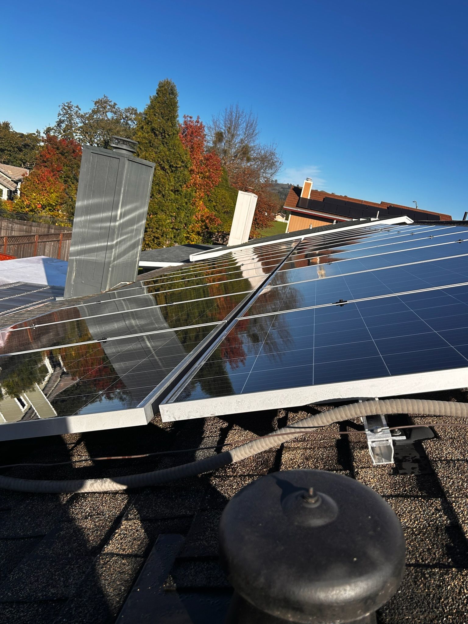 Solar panels on a roof, reflecting the sky and surrounding trees with colorful fall foliage.