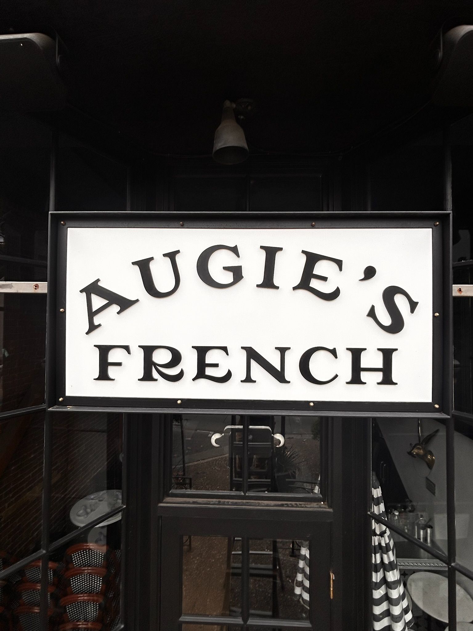 Sign for Augie's French restaurant, white with black lettering. The entrance is visible beneath the sign.