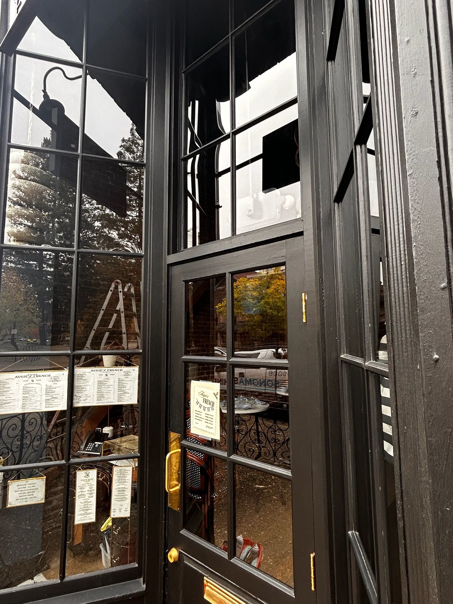 Black storefront entrance with glass panels. Displays and trees visible in the reflection.