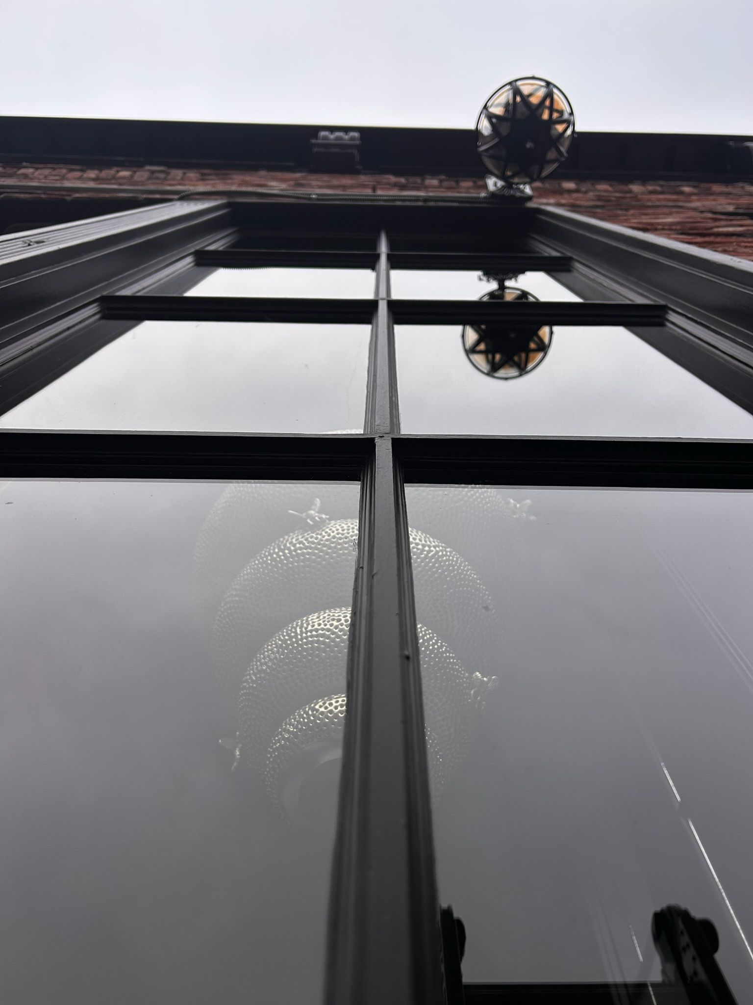Looking up at a window reflecting light, with a decorative sphere above. Brick building.
