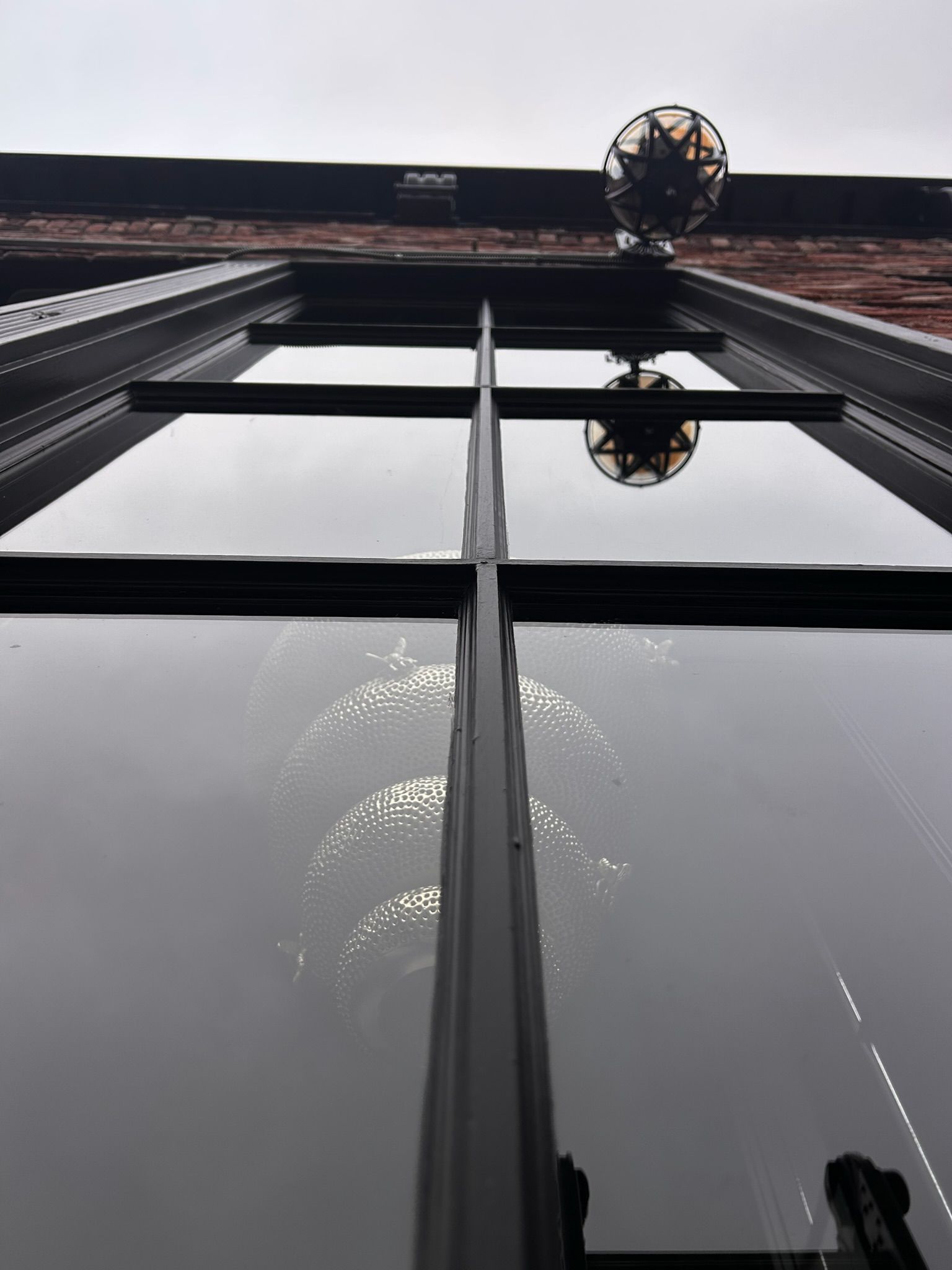 Low angle view of window reflecting light, with a hanging light fixture and brick building.
