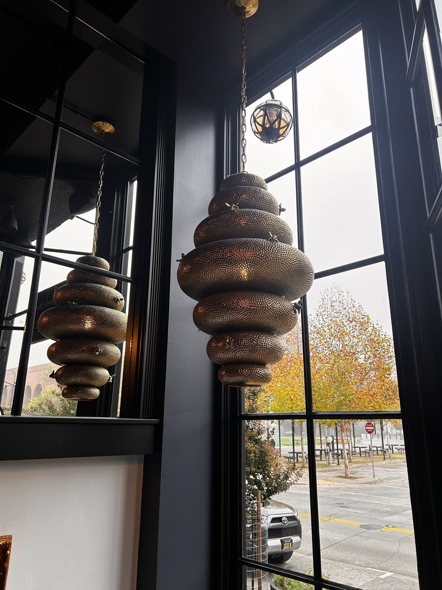 Two ornate gold chandeliers hang by a large window. Autumn trees and a street are visible outside.
