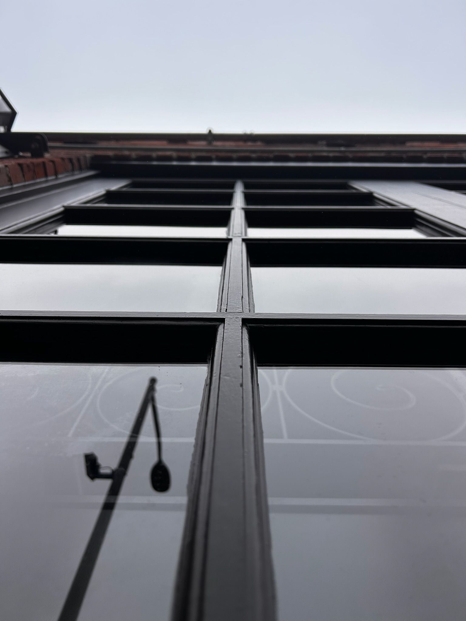 Low-angle view of a large window with black frames reflecting the sky and a street lamp.