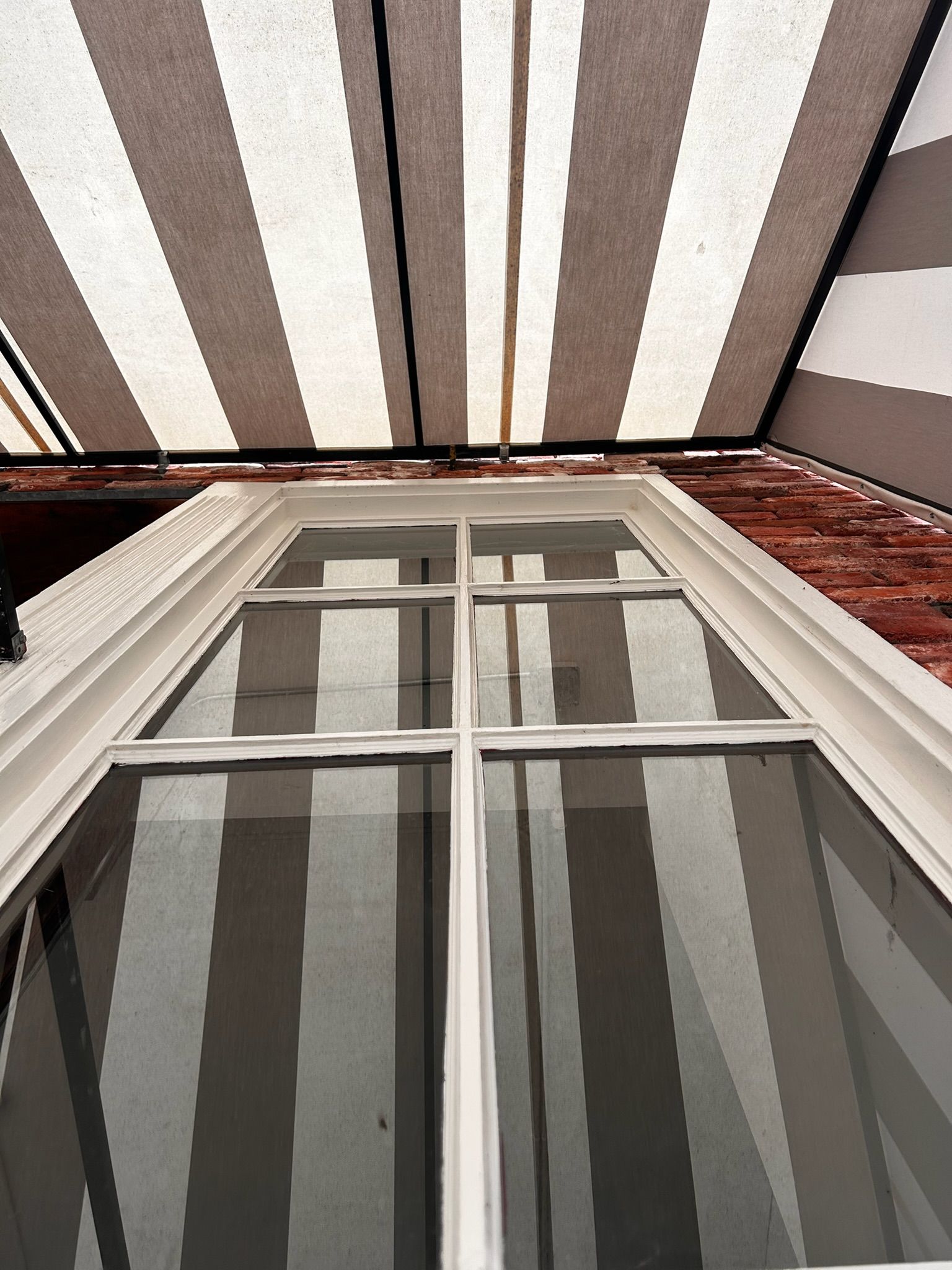 Window under a striped awning, brick wall. The window's glass reflects the awning's stripes.