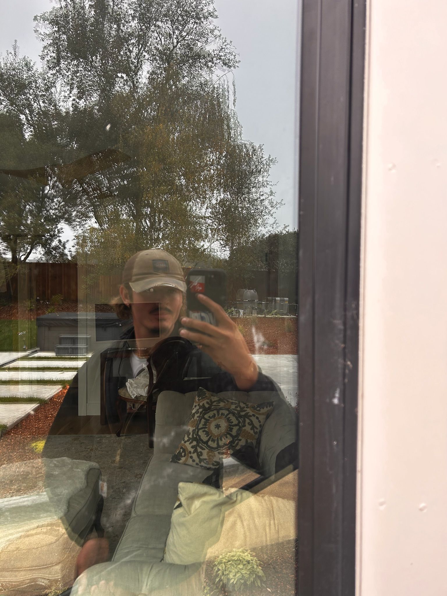 Person taking a selfie in a window, reflection shows outdoor scene.