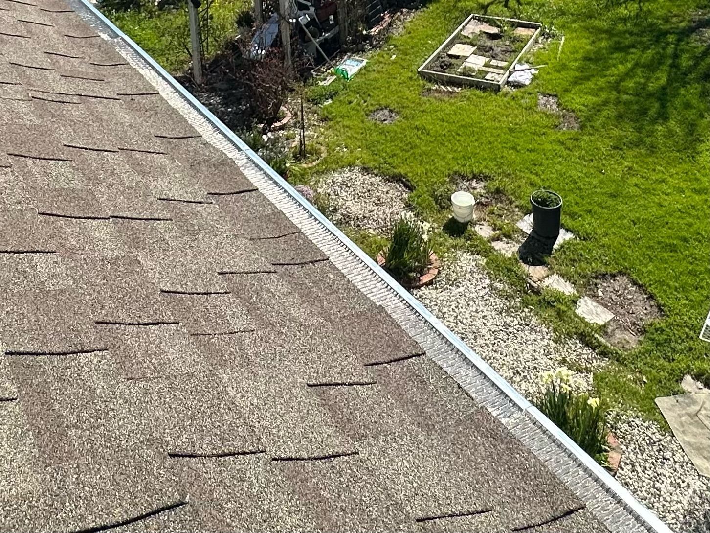 Roof with brown shingles, silver gutter, and backyard with grass and garden beds.