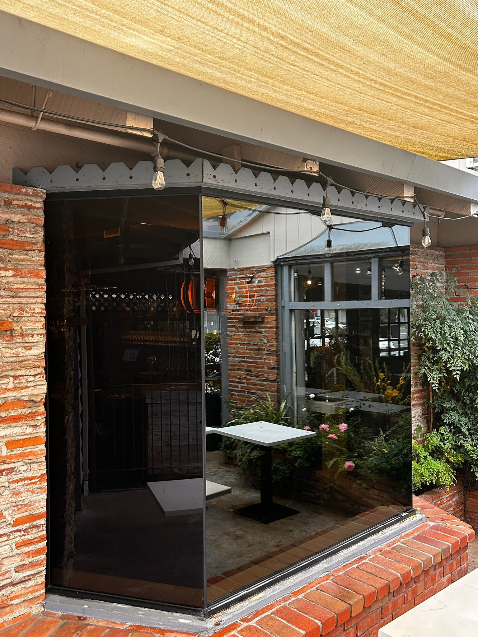 Exterior of a building with a black reflective glass wall, red brick and a white table visible within.