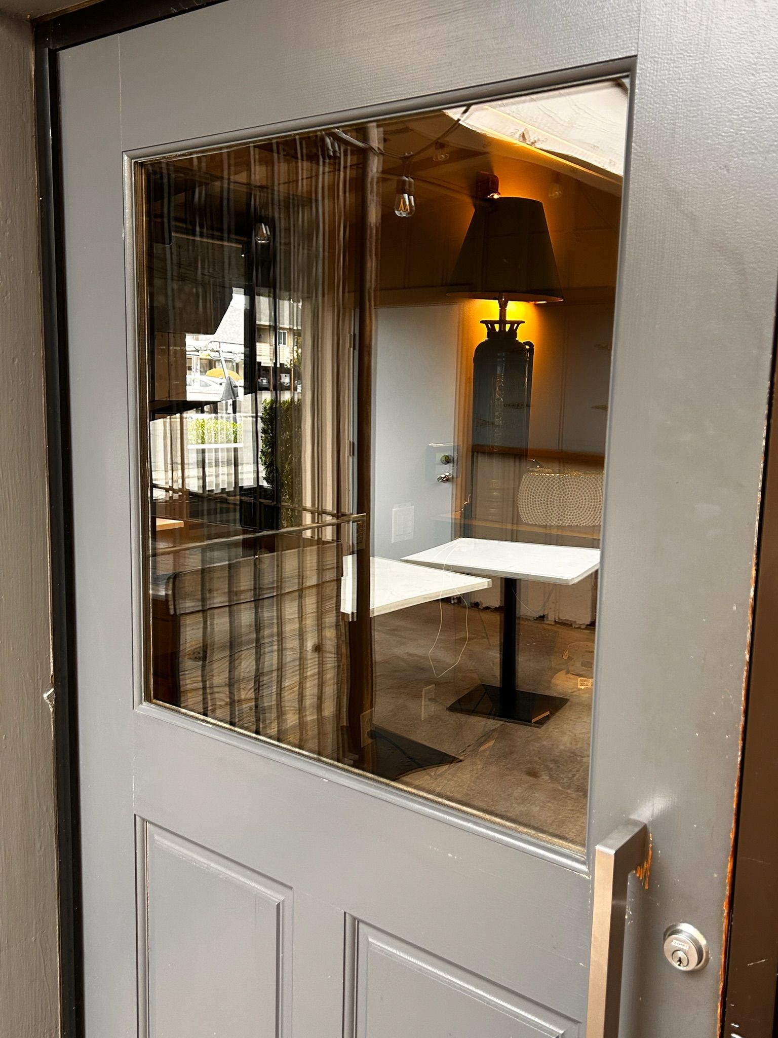Gray door with window, visible interior with tables, lamp, and metal grate.
