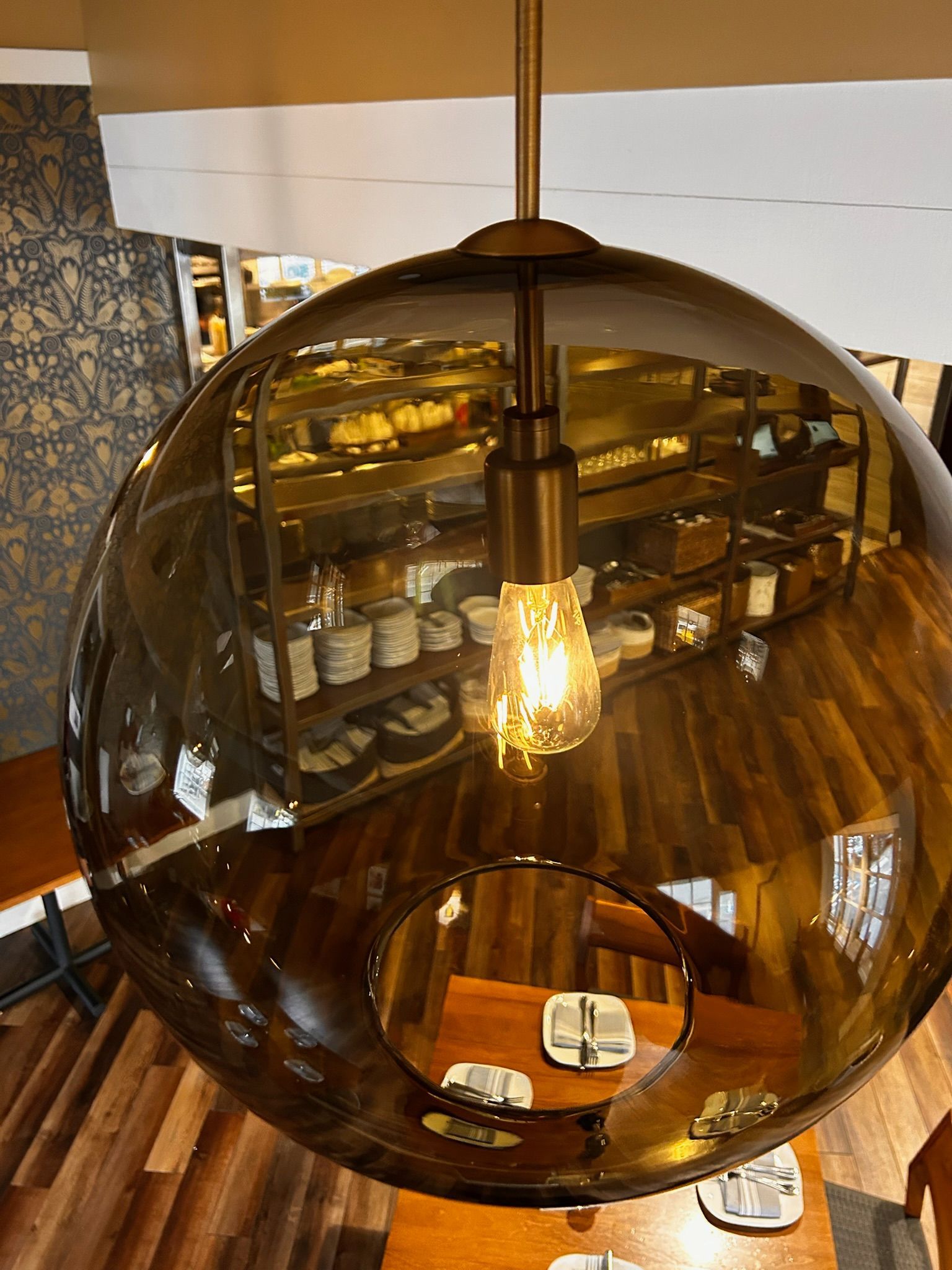 Overhead view of a dining room with a large, smoked glass globe pendant light. Wooden table and stairs visible.