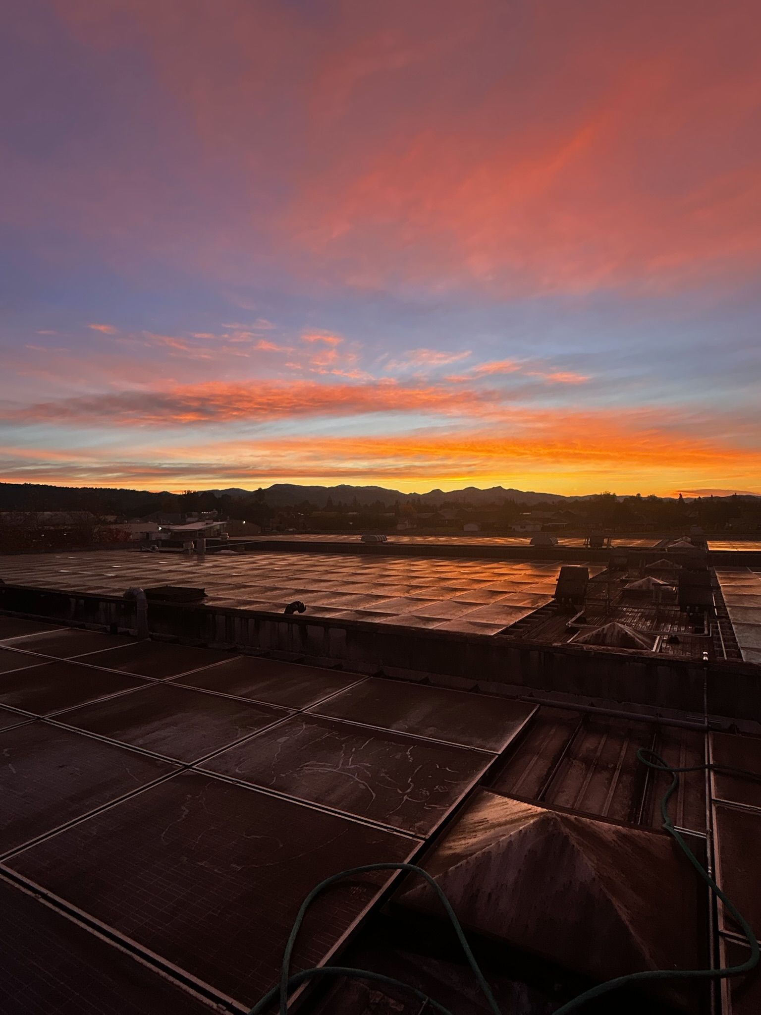 Sunrise over a harbor, with colorful sky reflected in water and dark foreground with industrial structures.