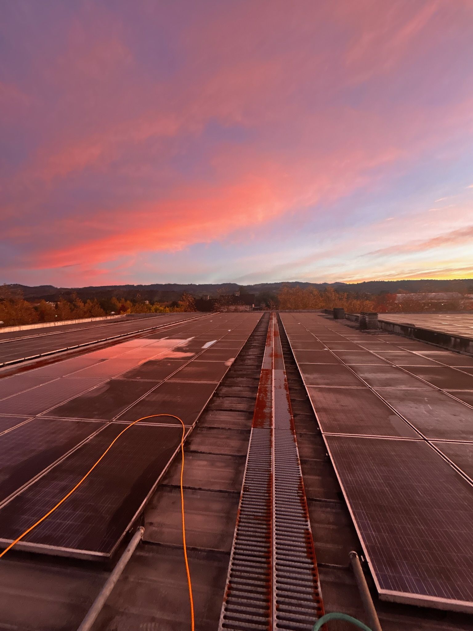 Rooftop solar panels under a vibrant pink and orange sunset sky.