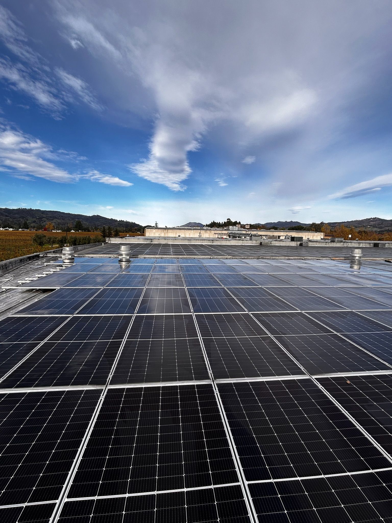 Solar panels on a building rooftop, with a cloudy blue sky in the background.