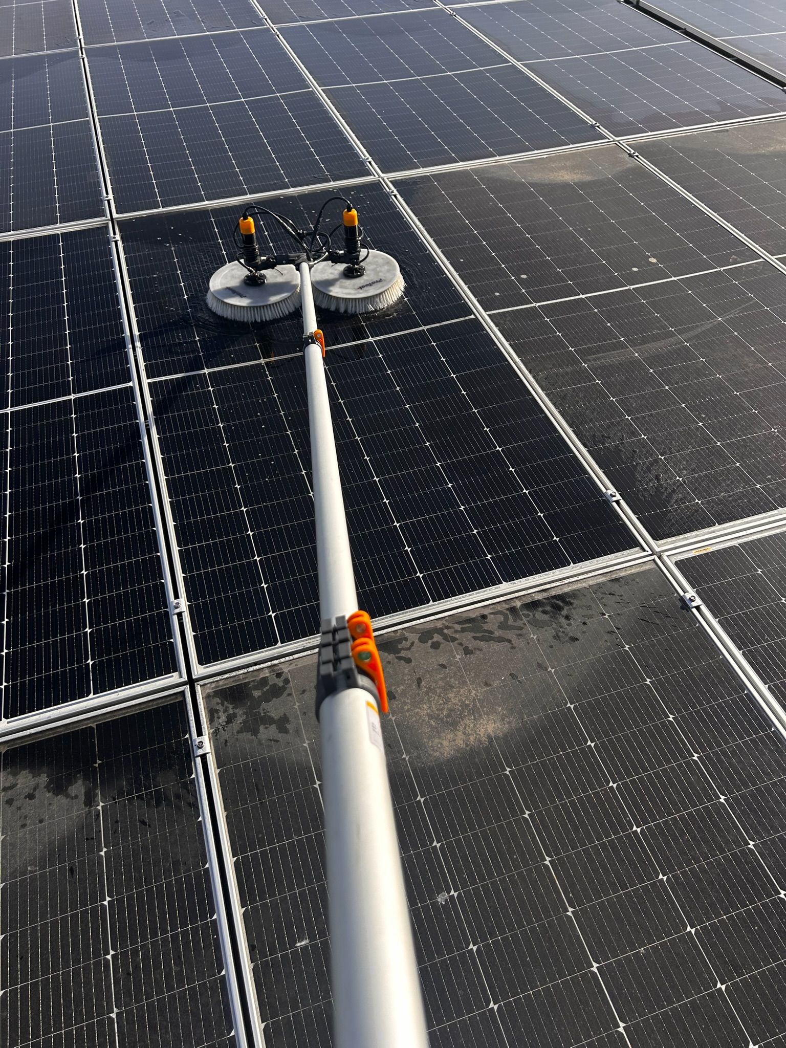 Solar panel being cleaned with a long-handled brush.