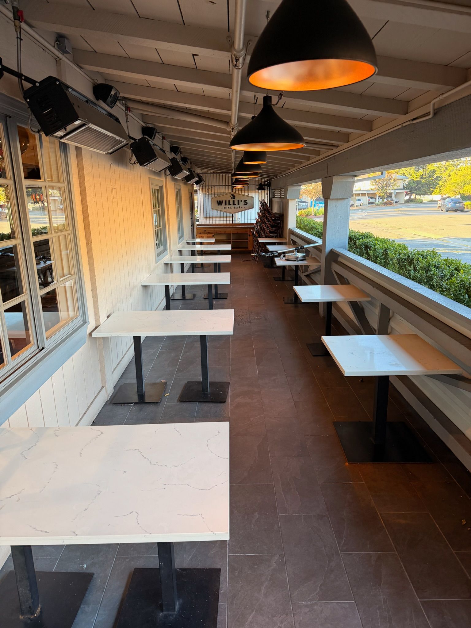 Outdoor restaurant seating area with white tables, black metal legs, and overhead lighting.