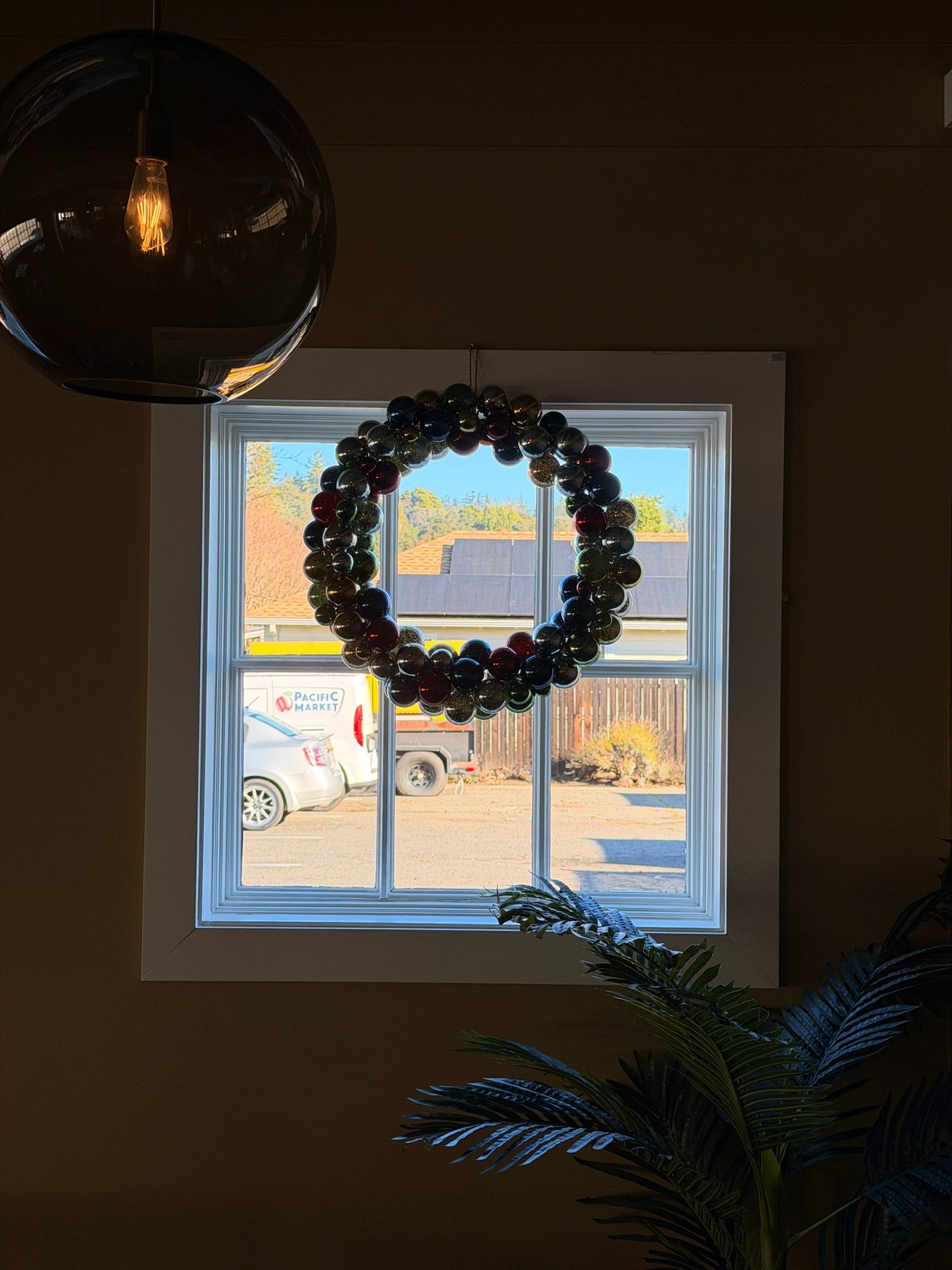 A window with a Christmas wreath, view of an outdoor scene, and a light fixture hanging from the ceiling.