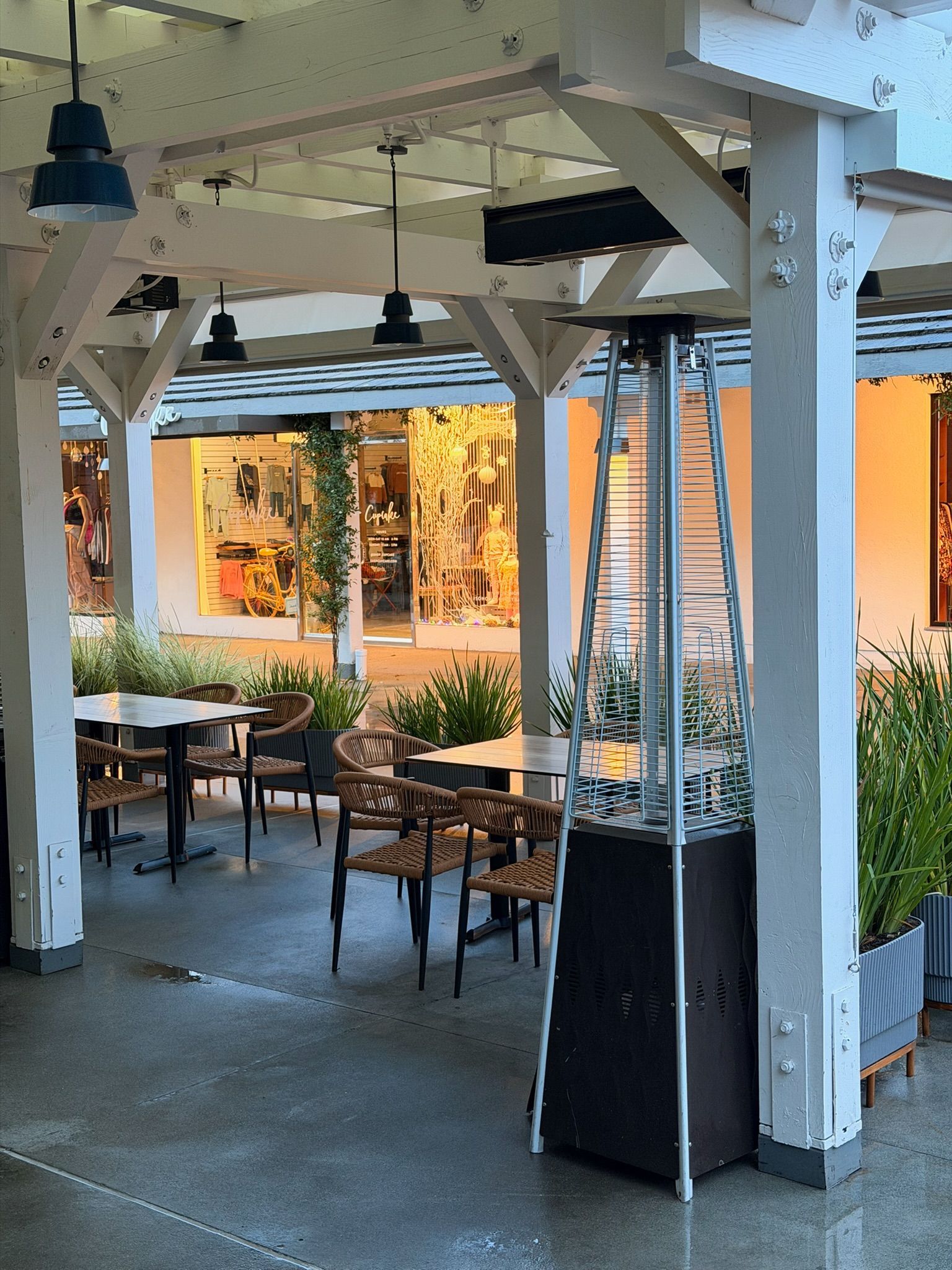 Outdoor restaurant patio with tables, chairs, and a gas heater beneath a white pergola.