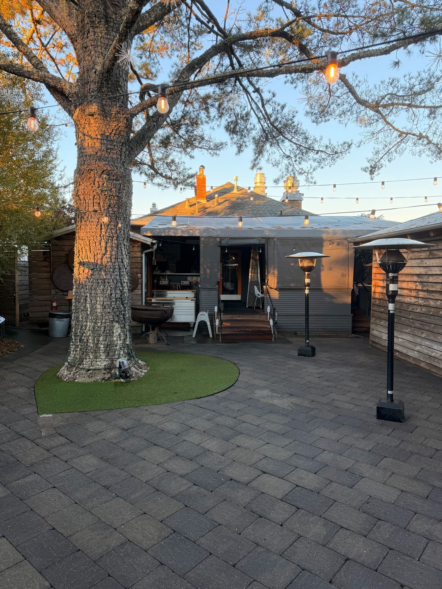 Outdoor dining patio with a tree, string lights, and patio heaters.