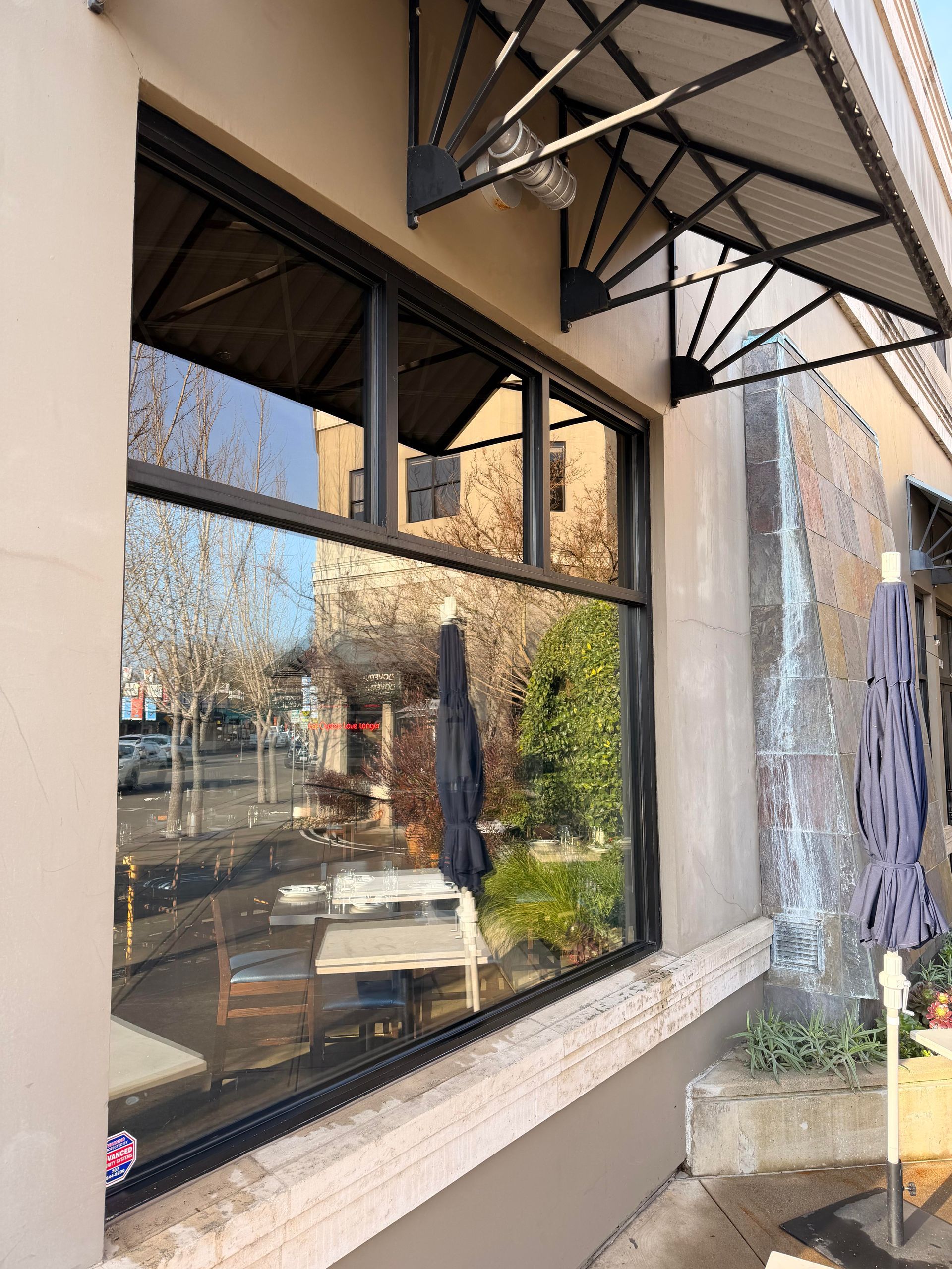 Building exterior with large windows reflecting outdoor seating and an awning.