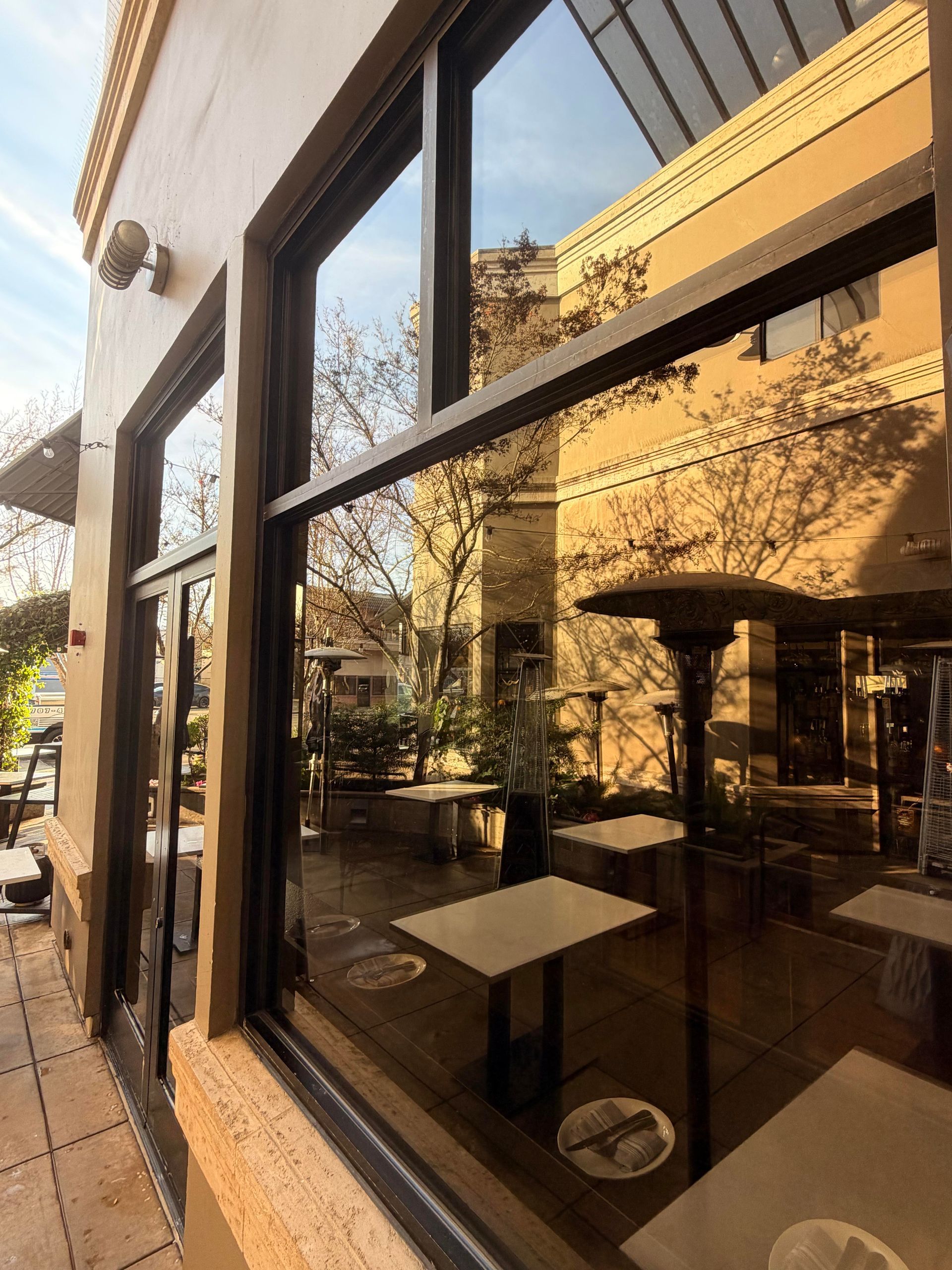 Restaurant exterior with large windows reflecting an outdoor patio with tables and a heater.