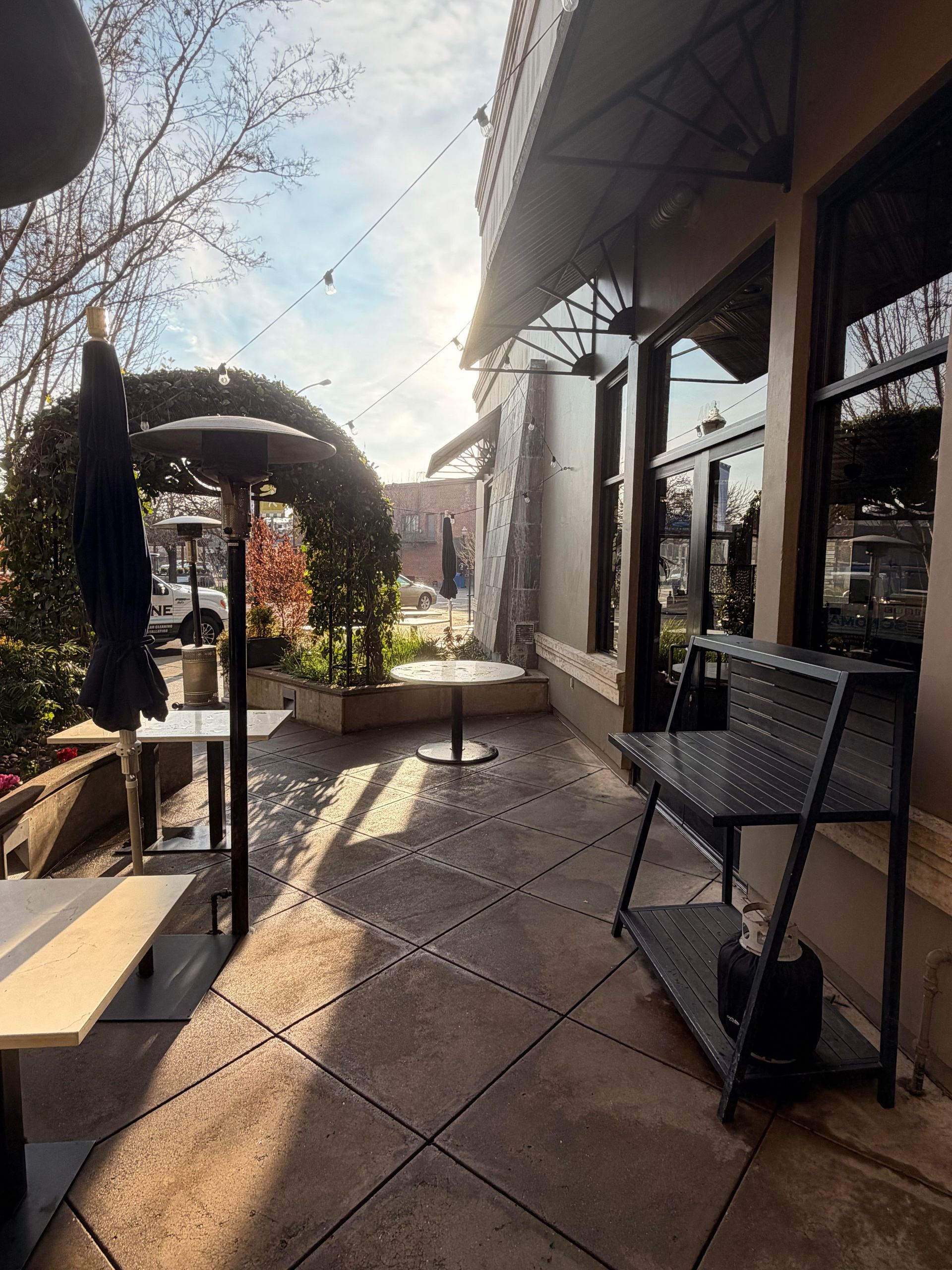 Outdoor restaurant patio with tables, bench, and an archway; sunny day.