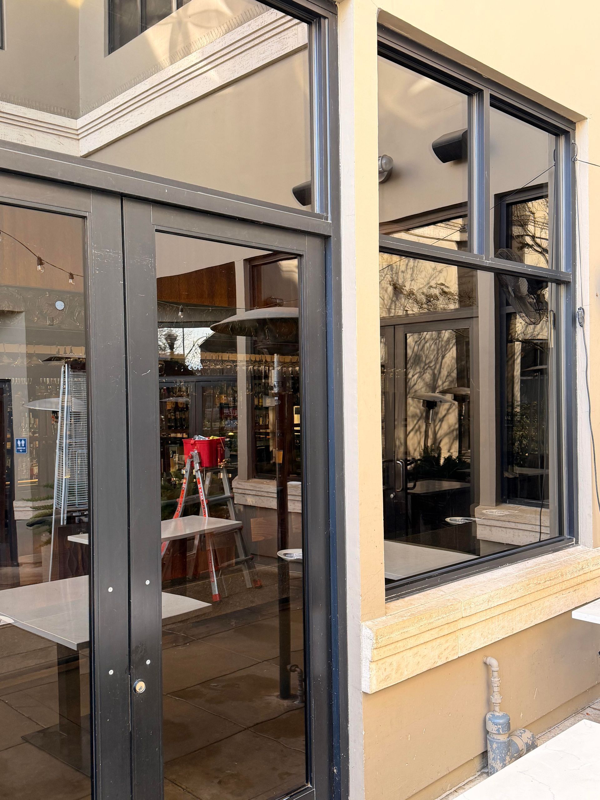 Exterior of a building with glass doors and windows, reflecting interior items and a ladder.