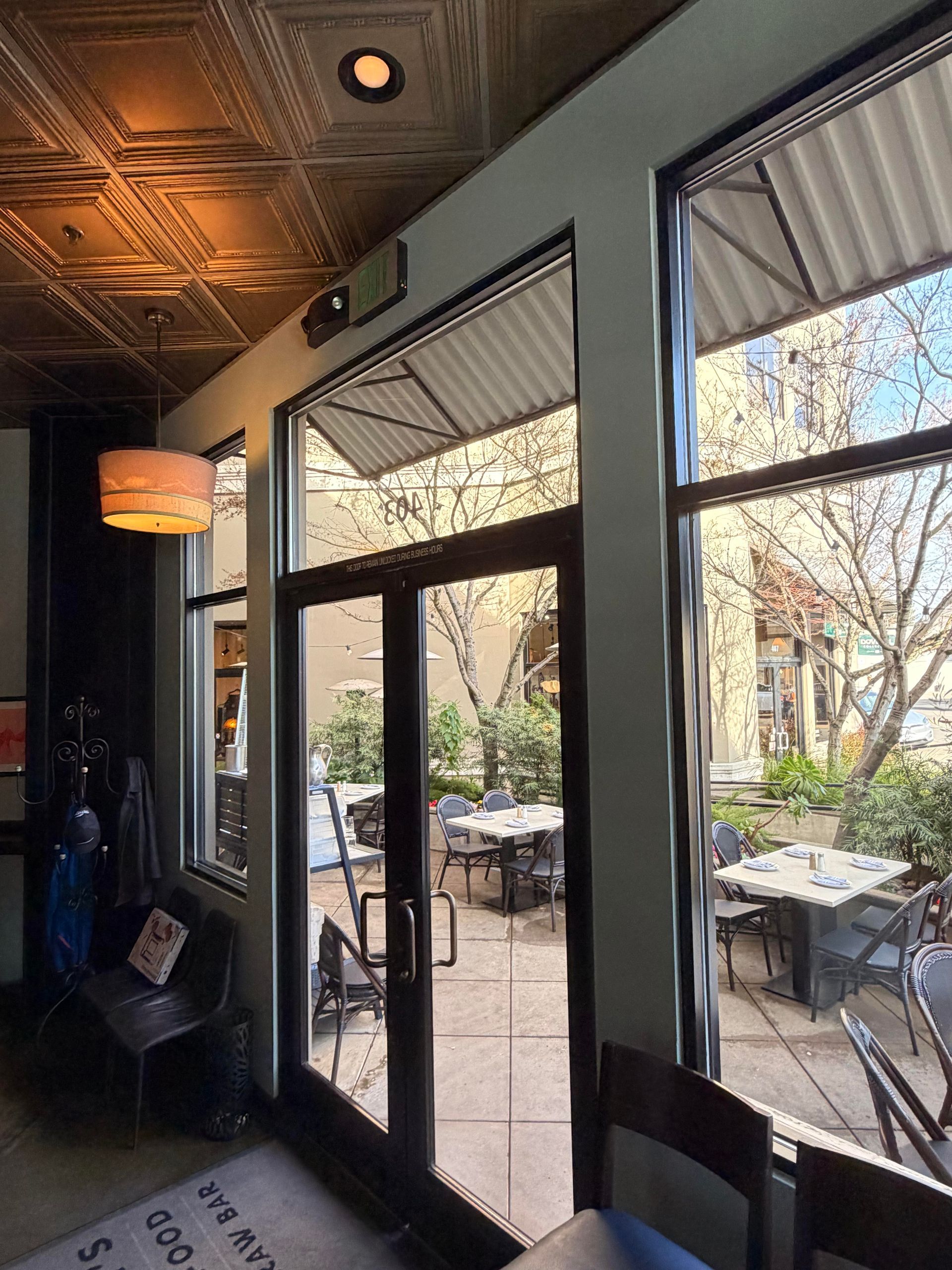 Interior view of a restaurant with a patio. Tables and chairs are outside the glass doors.