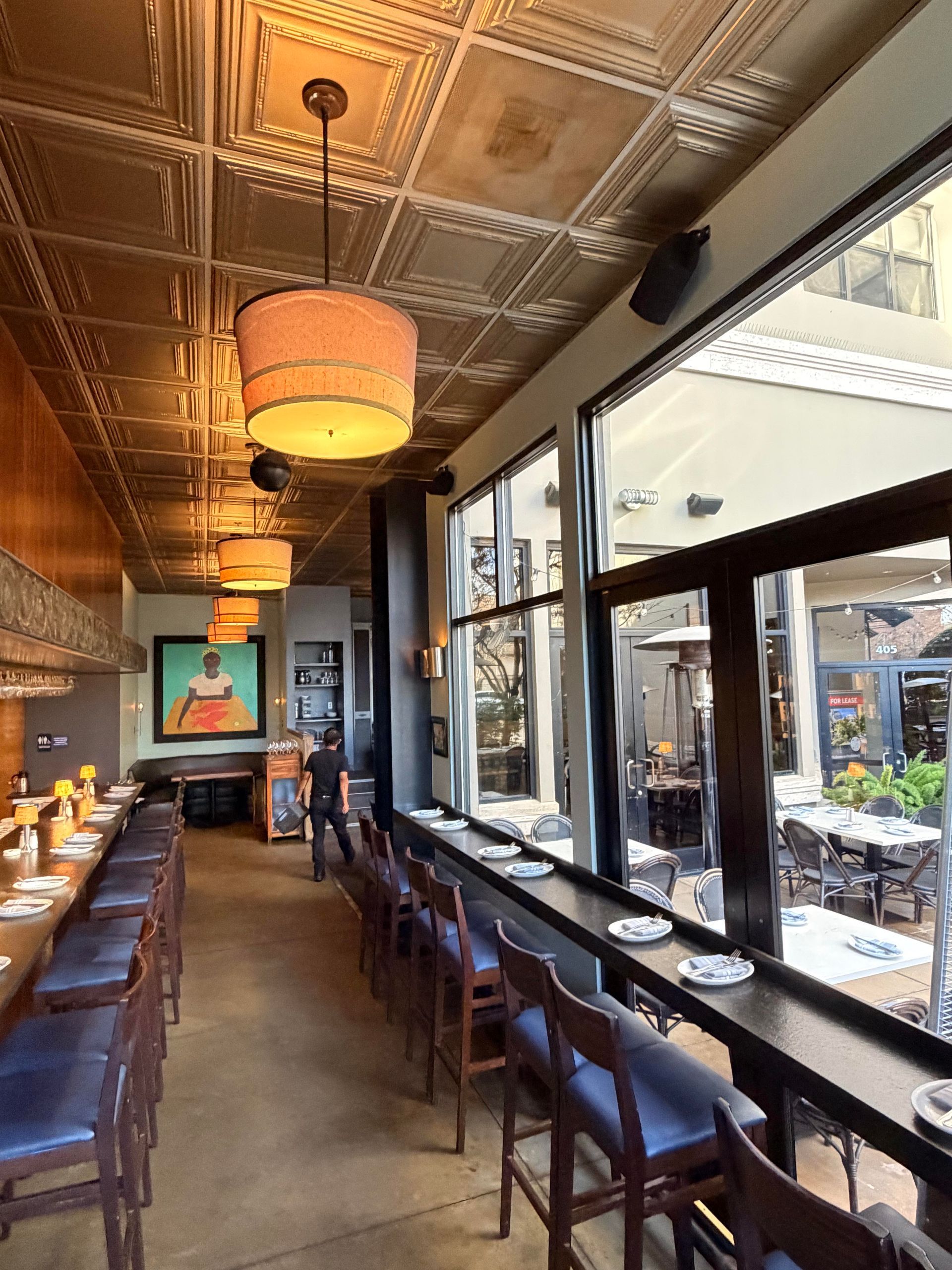 Interior restaurant view, counter seating along large windows, decorative ceiling, and pendant lights.