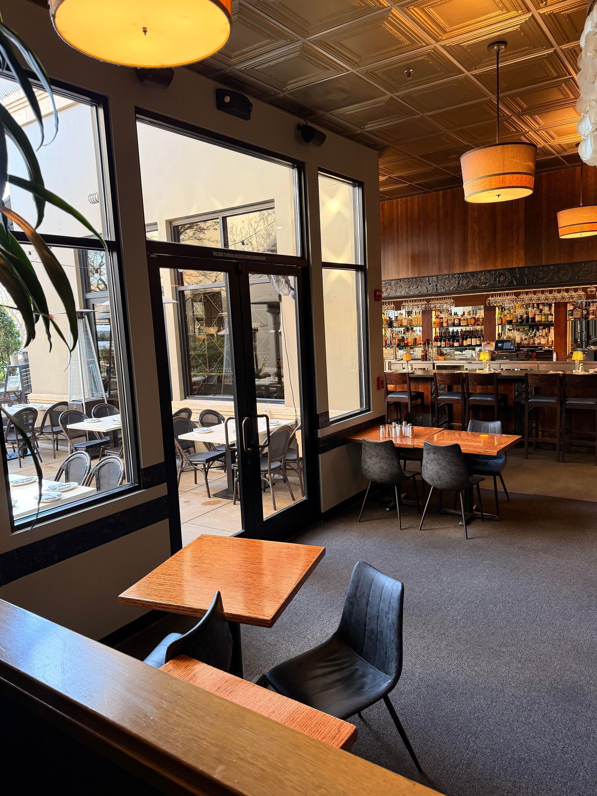 Restaurant interior with tables, chairs, bar, and outdoor seating visible through windows.