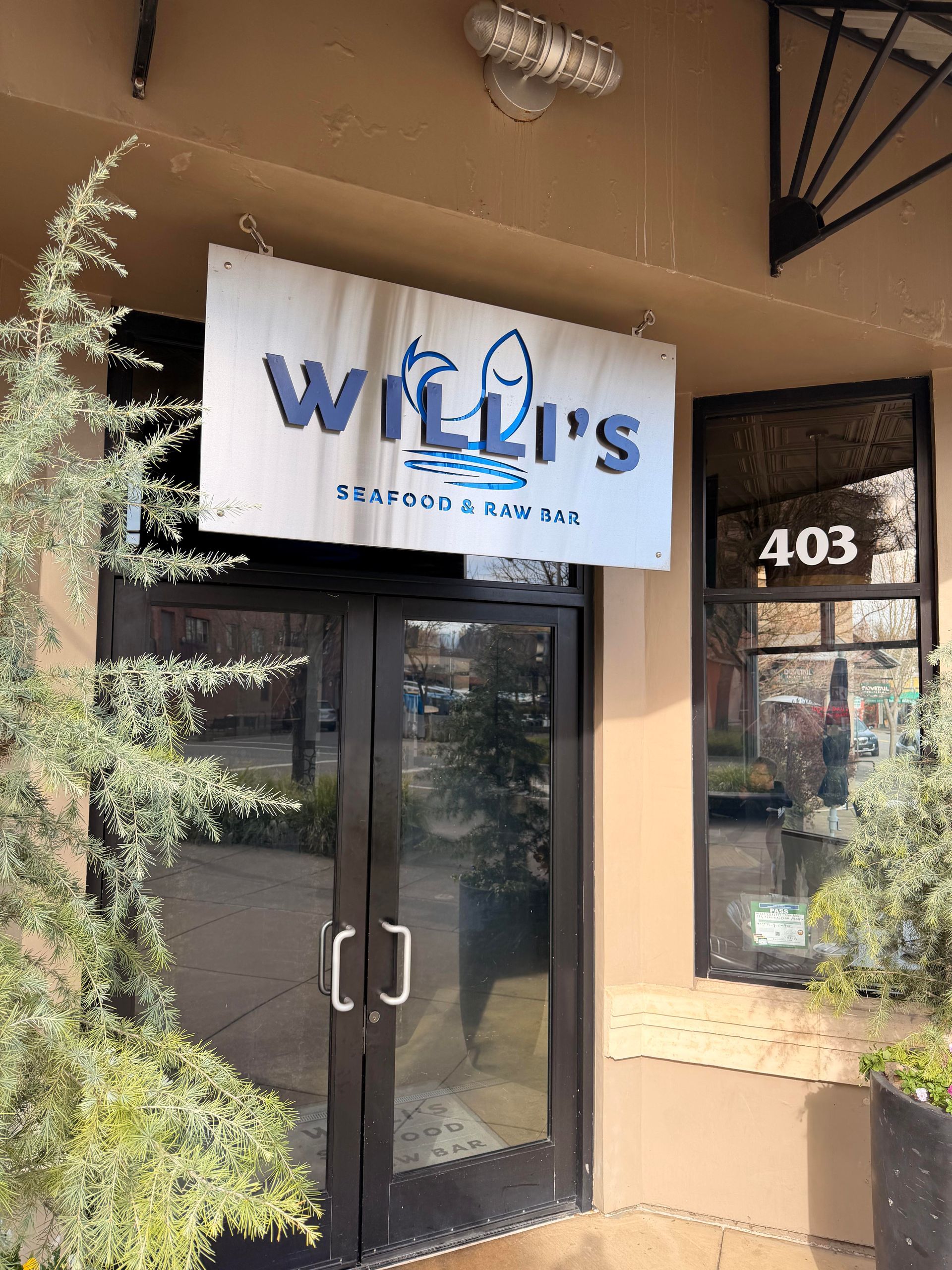 Willi's Surfside Bar and Grill storefront. Sign over black door, building number 403 visible, plants on either side.