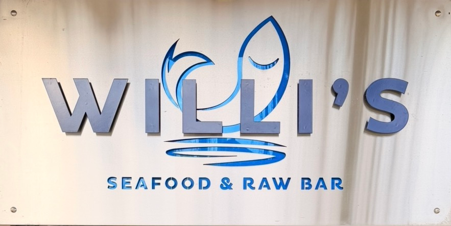 Sign for Willi's Seafood & Raw Bar. Blue lettering and logo on a light-colored background.