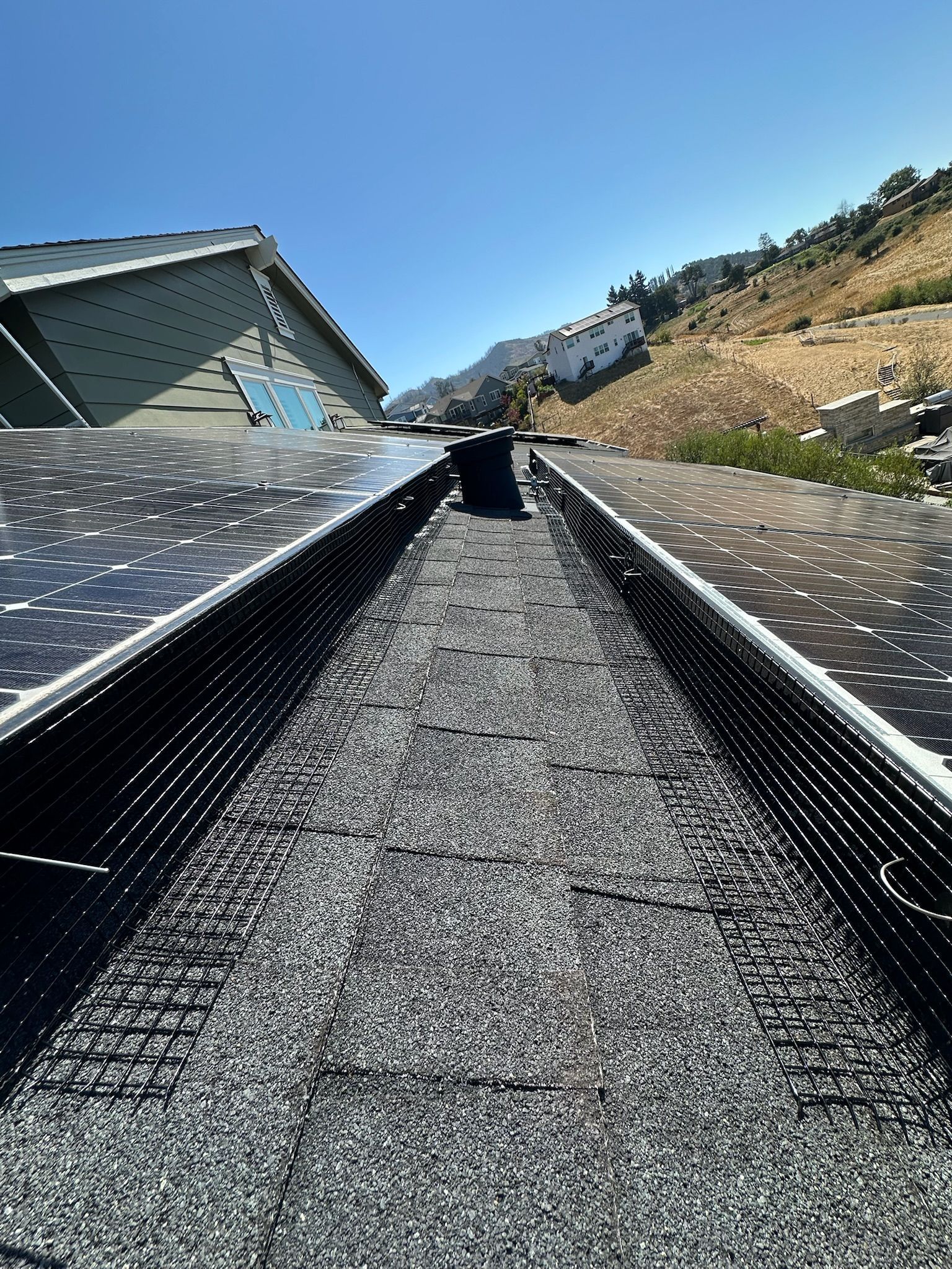 Solar panels on a roof, gravel channel. Mountain in the background. Clear sky.
