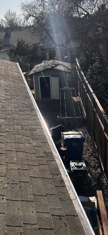 A high-angle view of a gray shingle roof, a shed, and an alleyway with a wooden fence.