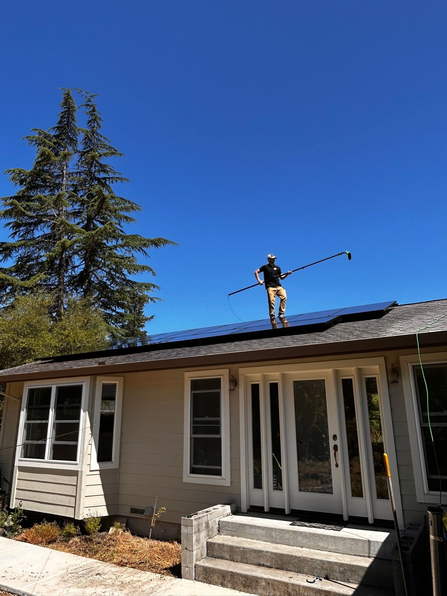Person on rooftop with solar panels, cleaning them with a long-handled brush on a sunny day.