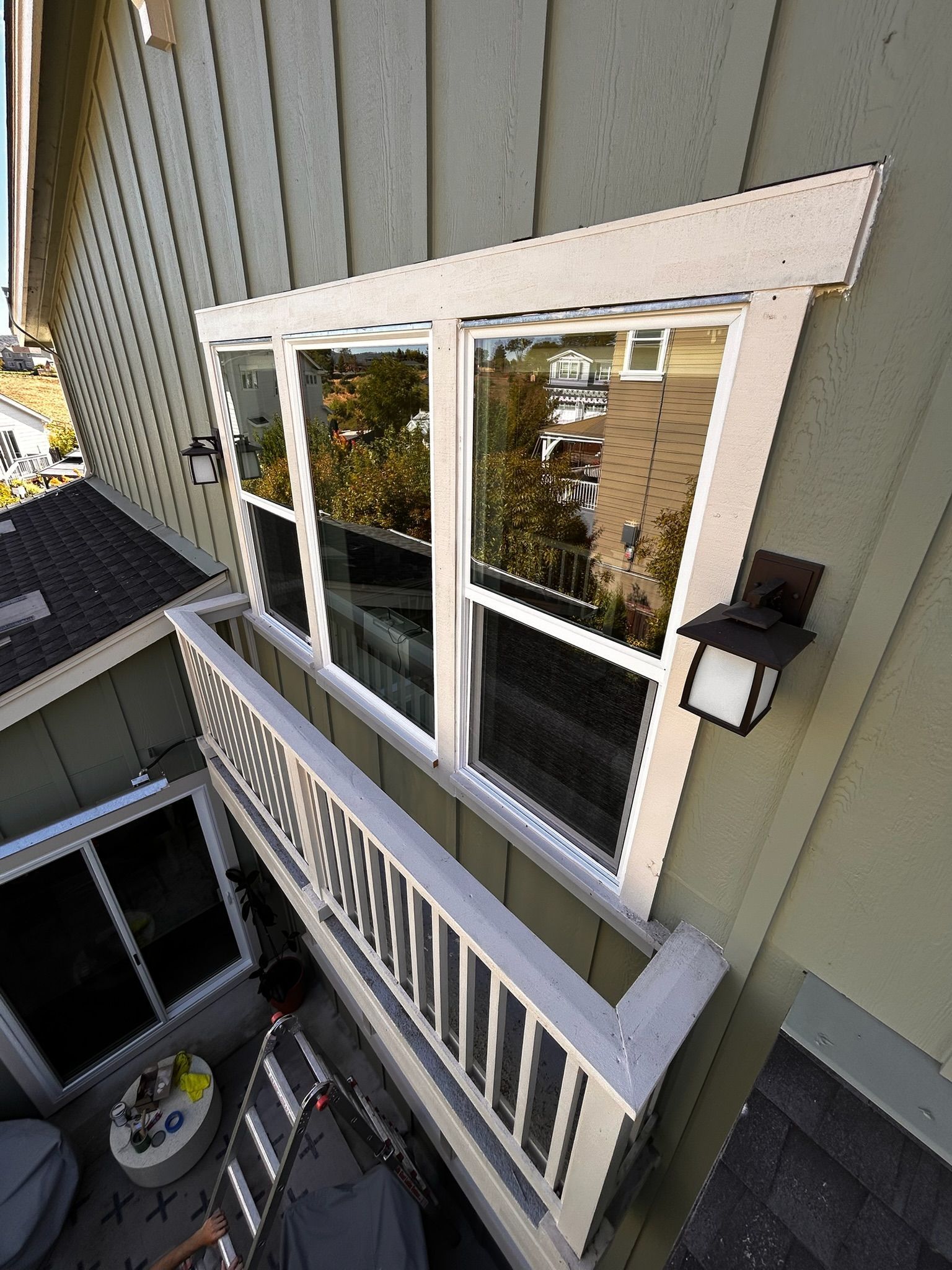 Windows on balcony with white trim. Reflecting trees, a house, and an exterior light fixture on a green wall.