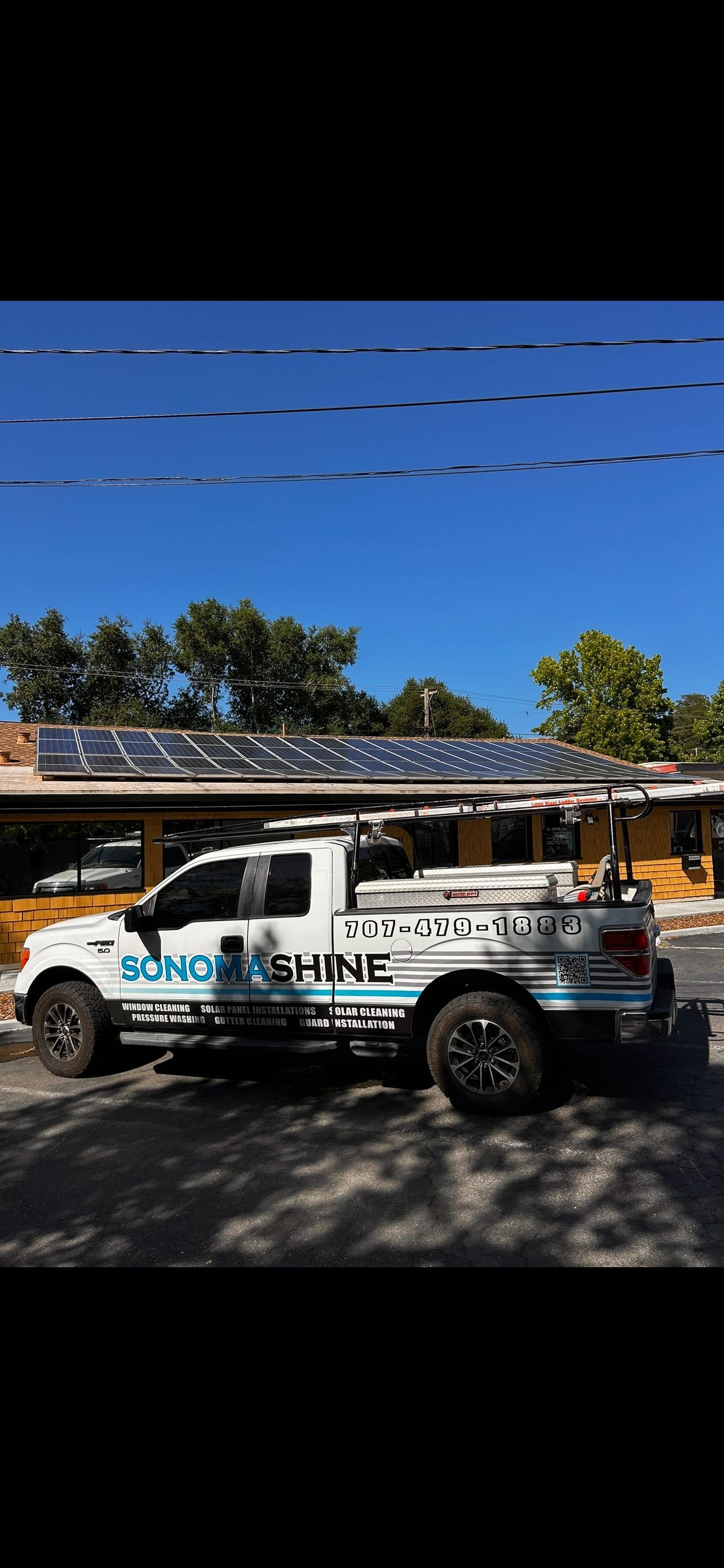 Solar panel installation truck parked in front of building with installed solar panels on roof. Sunny day.