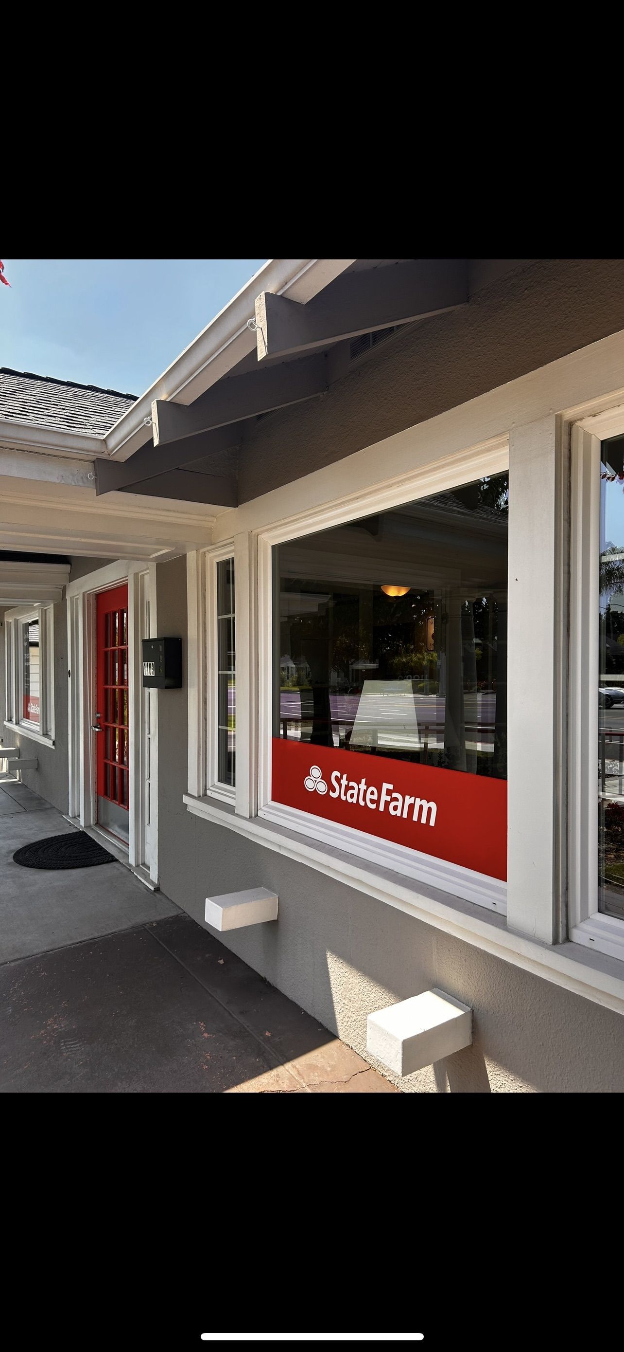 Exterior of a State Farm insurance office with a red door and a sign in the window.