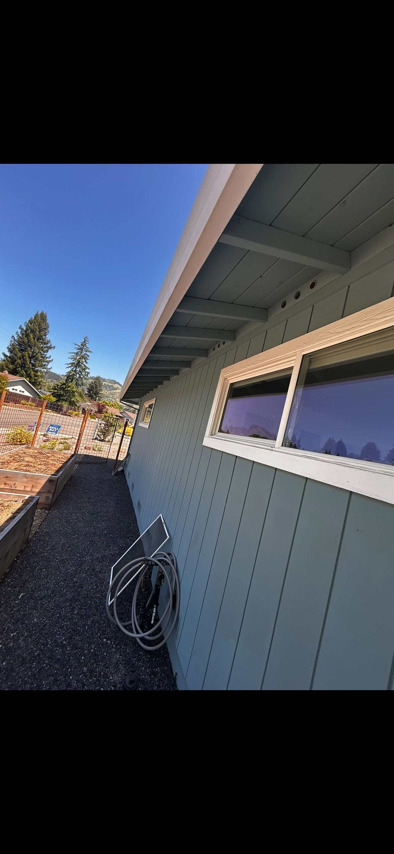 Side of a light blue house with a window, black gravel, and a blue sky.