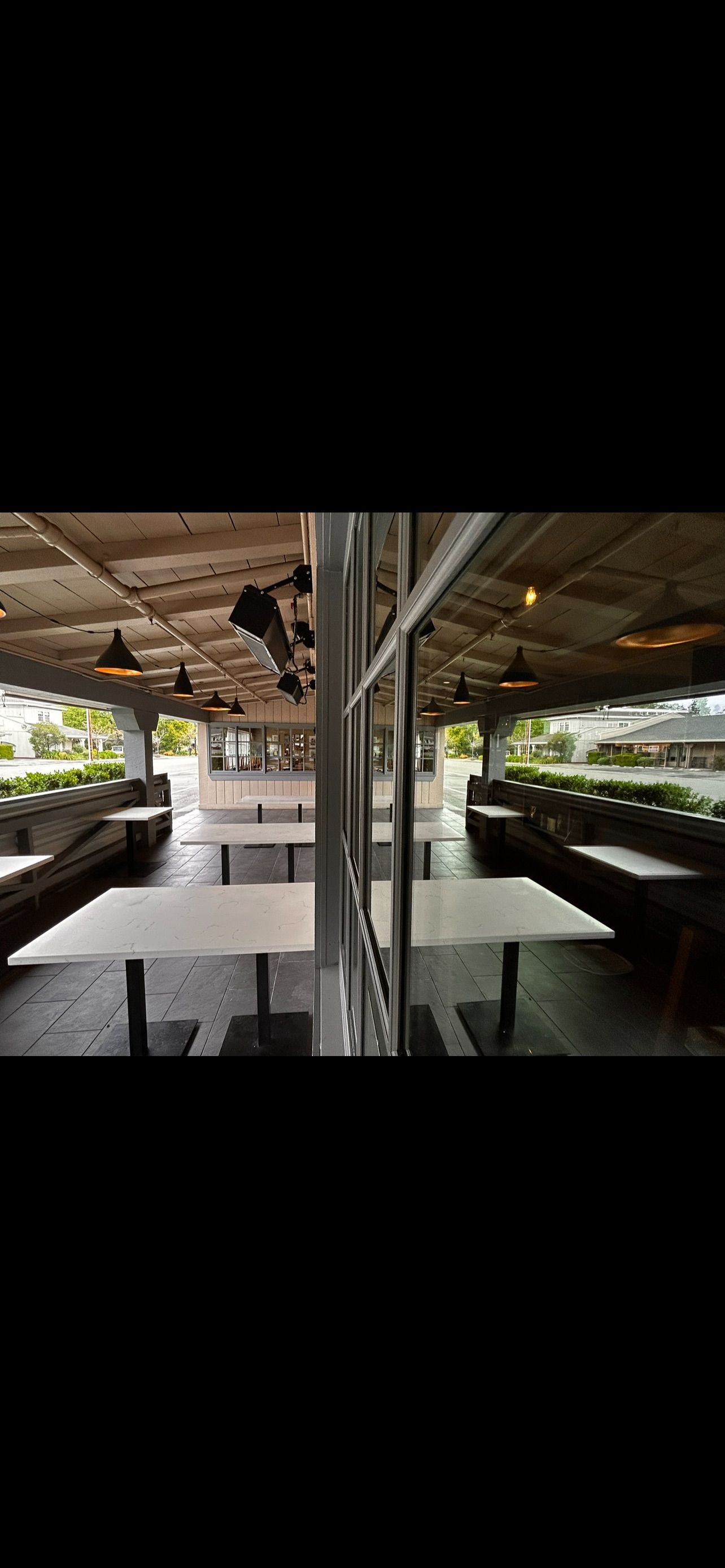 An empty outdoor dining area with white tables and dark seating under a wooden roof.