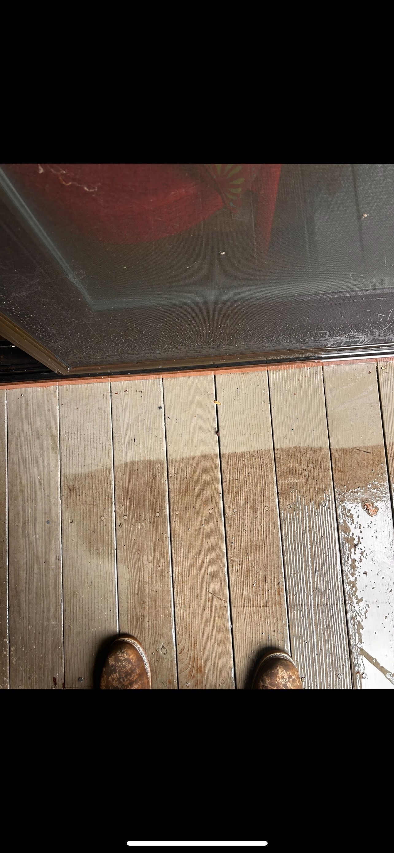 Person standing on wet wooden planks near a dark object, likely an appliance or structure.