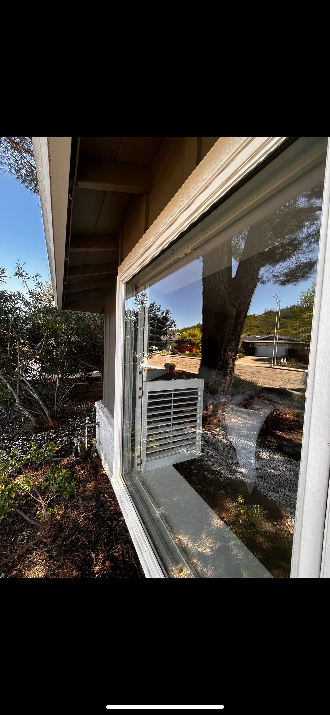 Exterior view of a window reflecting the outside. A metal vent is visible behind the glass.