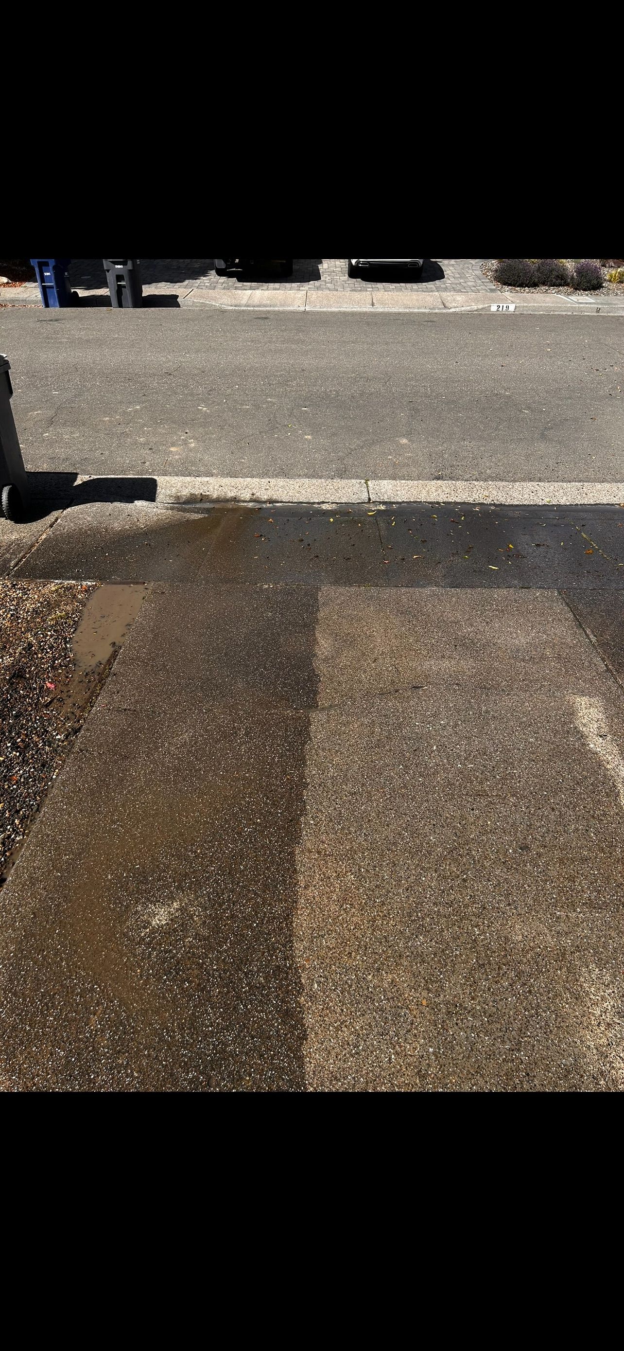A wet, cleaned asphalt section contrasts with a dry, dirty section of pavement.