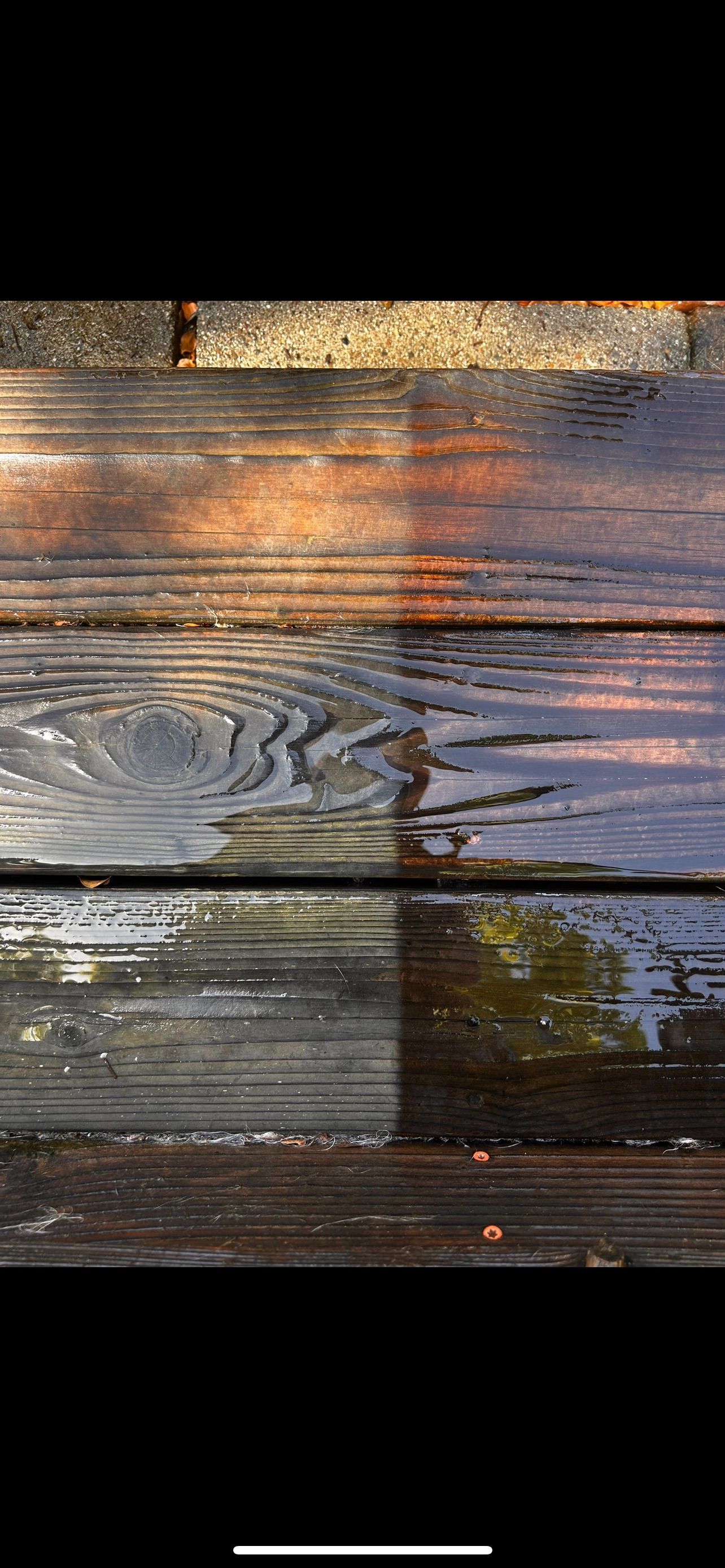 Wet wooden planks, possibly a deck, with sunlight reflections and a black background.