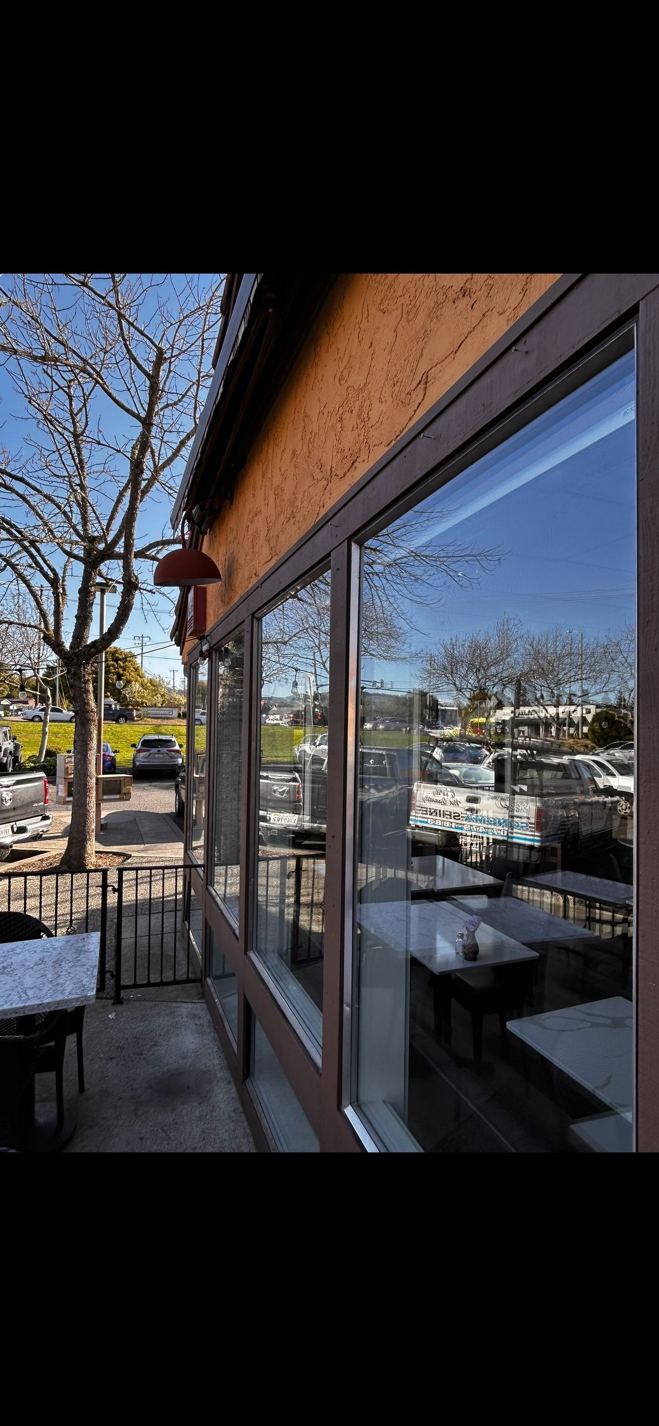 Exterior of a restaurant with a patio, reflecting trees and sky in its windows.