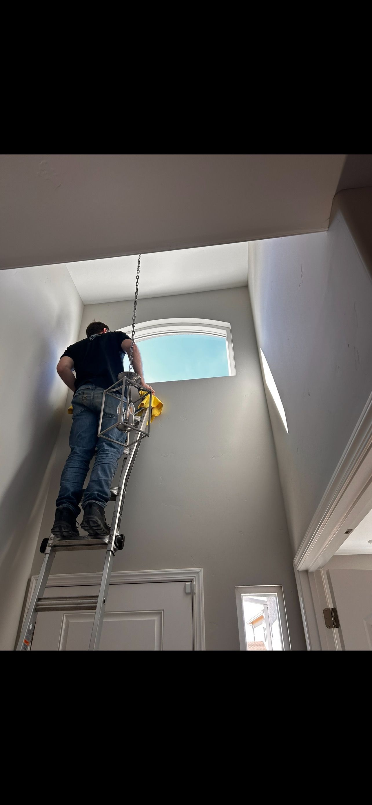Person on a ladder working on a high window inside a building.